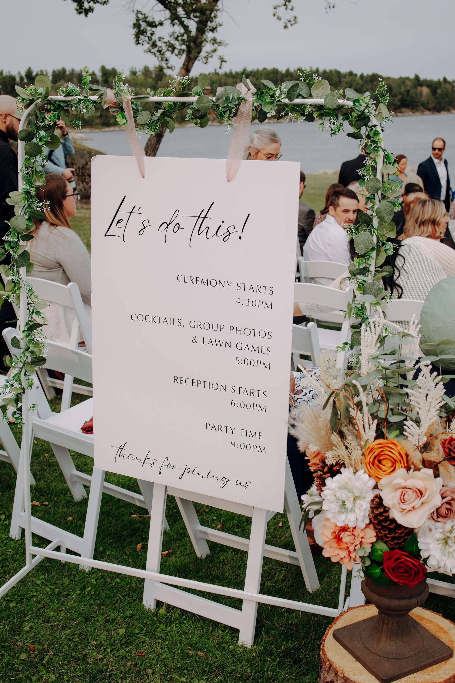 Wedding ceremony signage displays timeline details with floral decorations on white chairs.