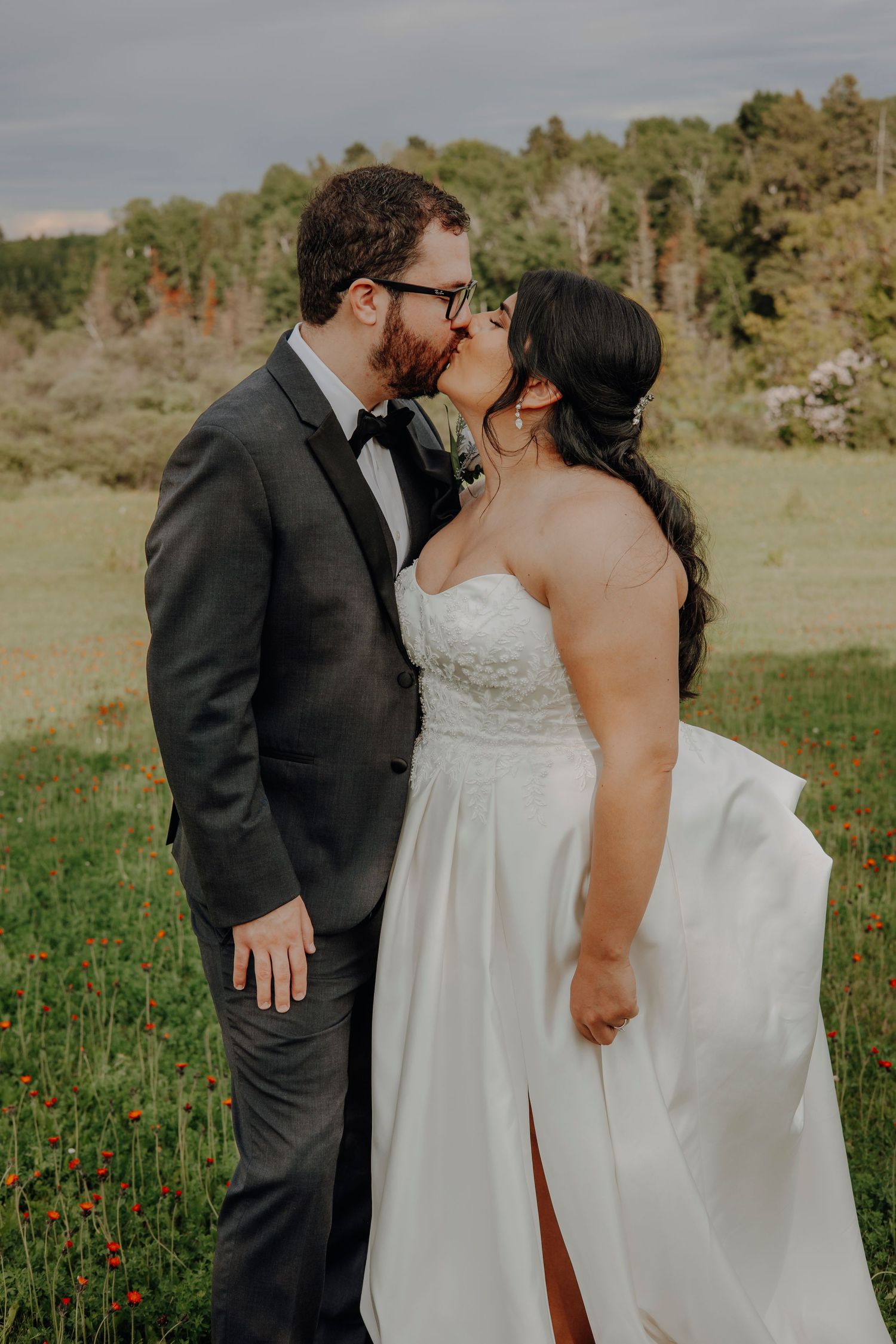 Romantic wedding couple shares tender moments in a field with evergreen trees.