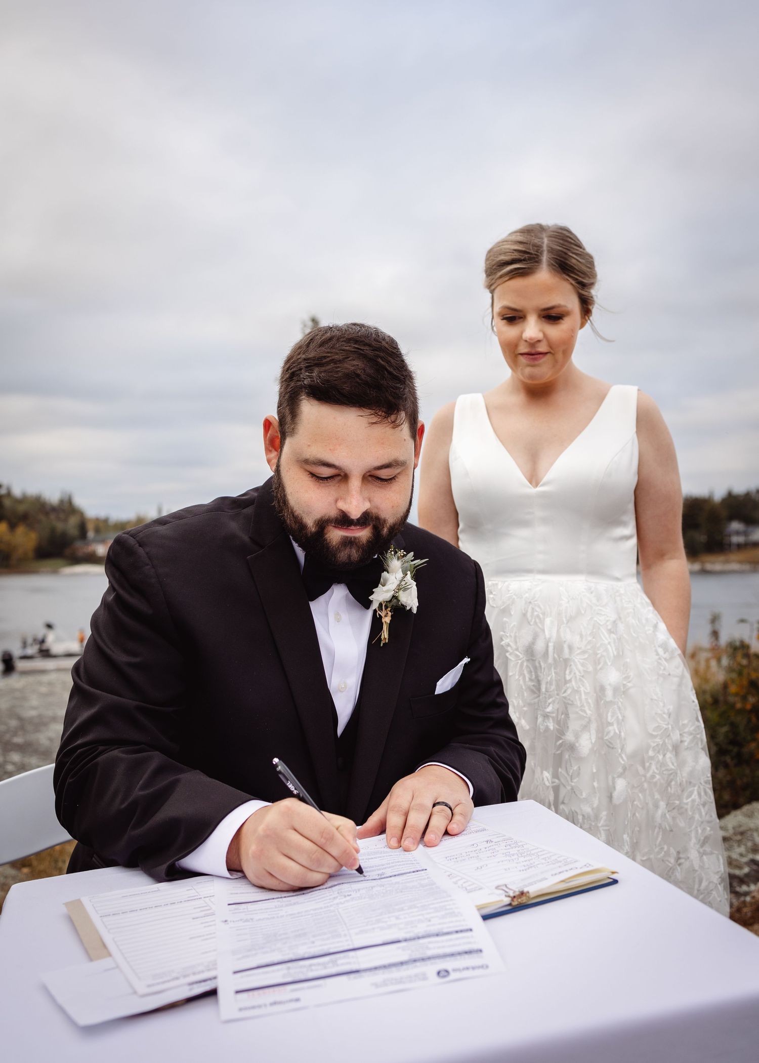 Wedding ceremony document signing with couple at waterfront location.