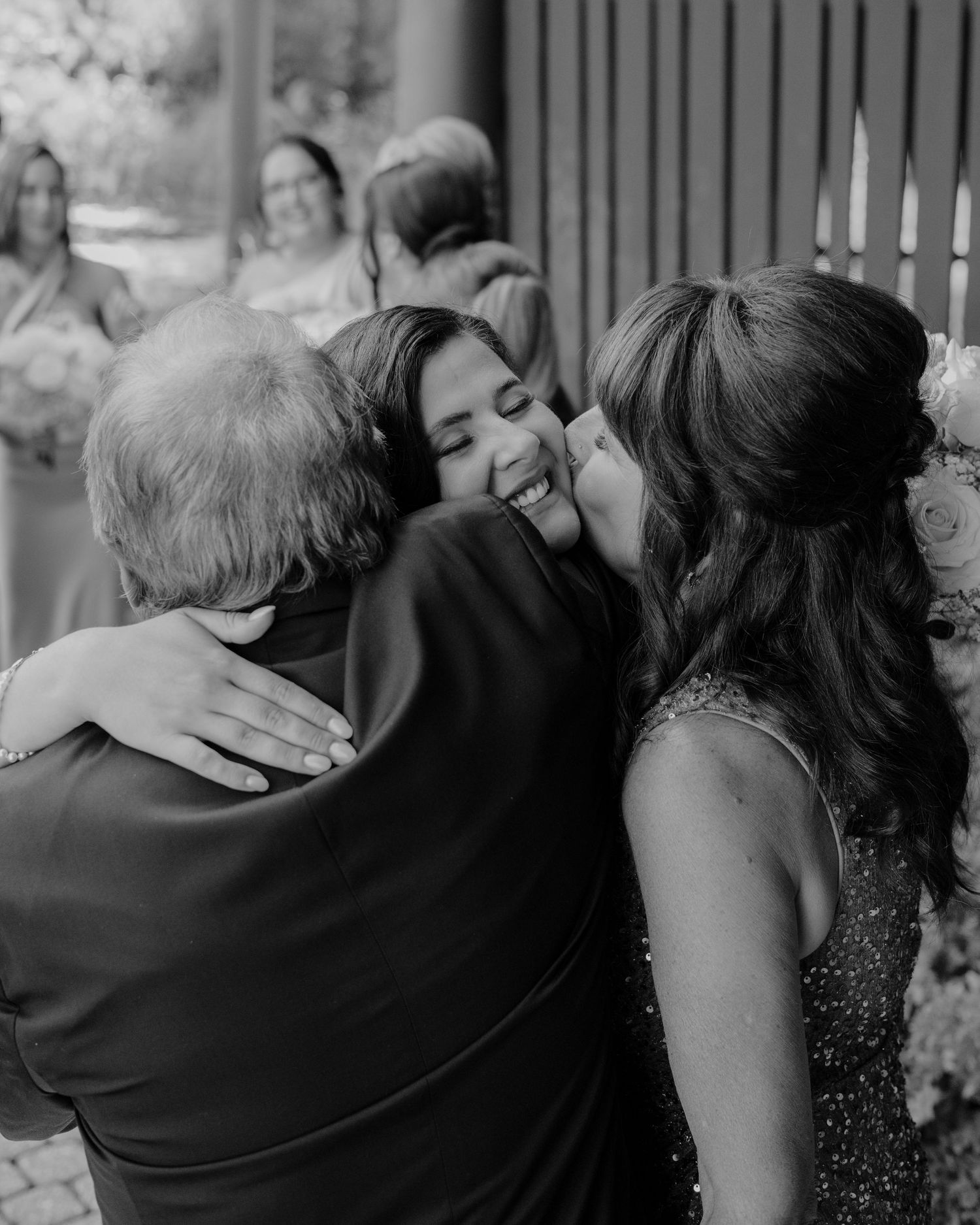 Black and white candid photograph capturing an intimate embrace between loved ones sharing an emotional moment at a celebration.