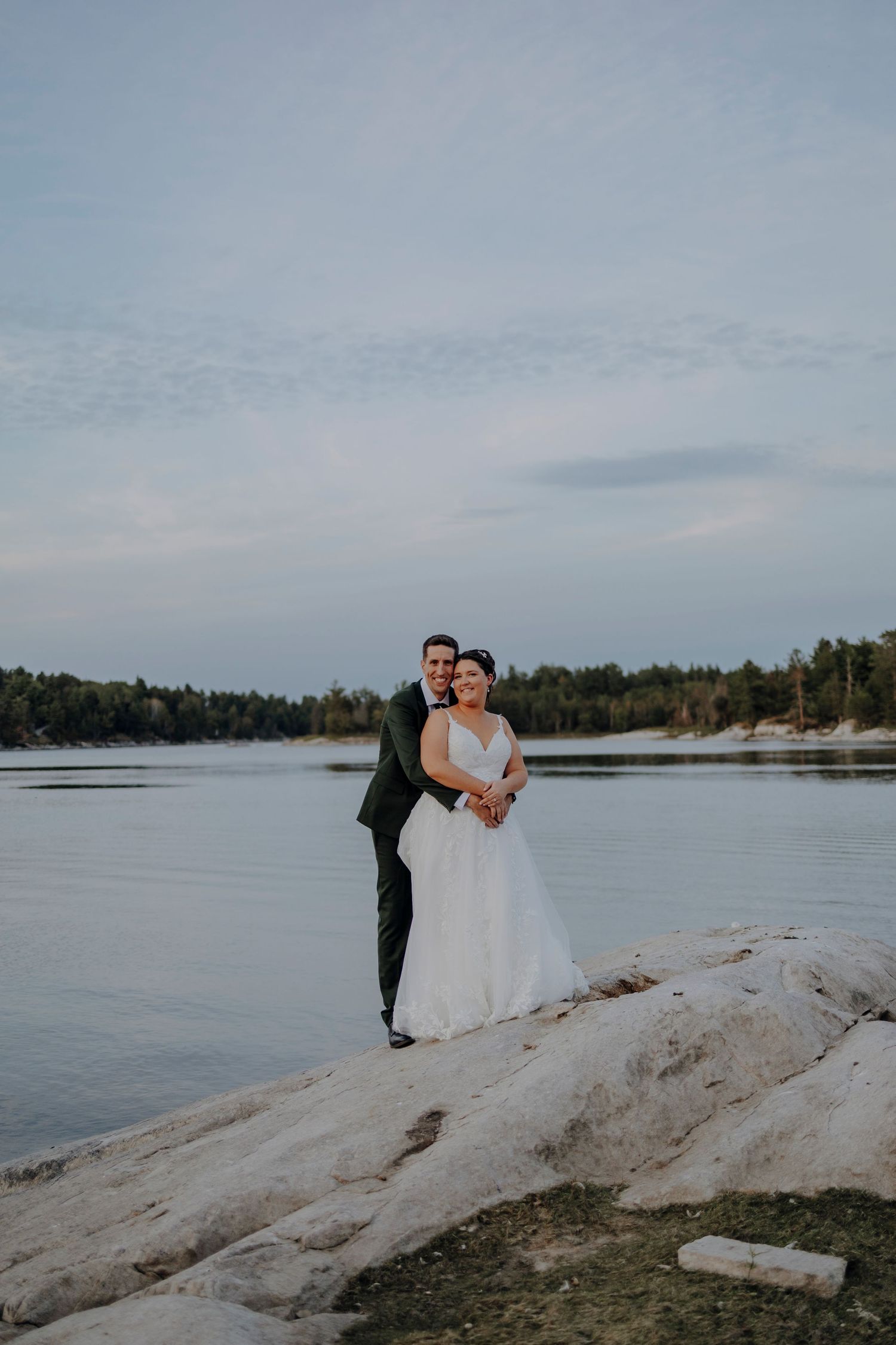 Couple poses for romantic photos on rocky shoreline at sunset.
