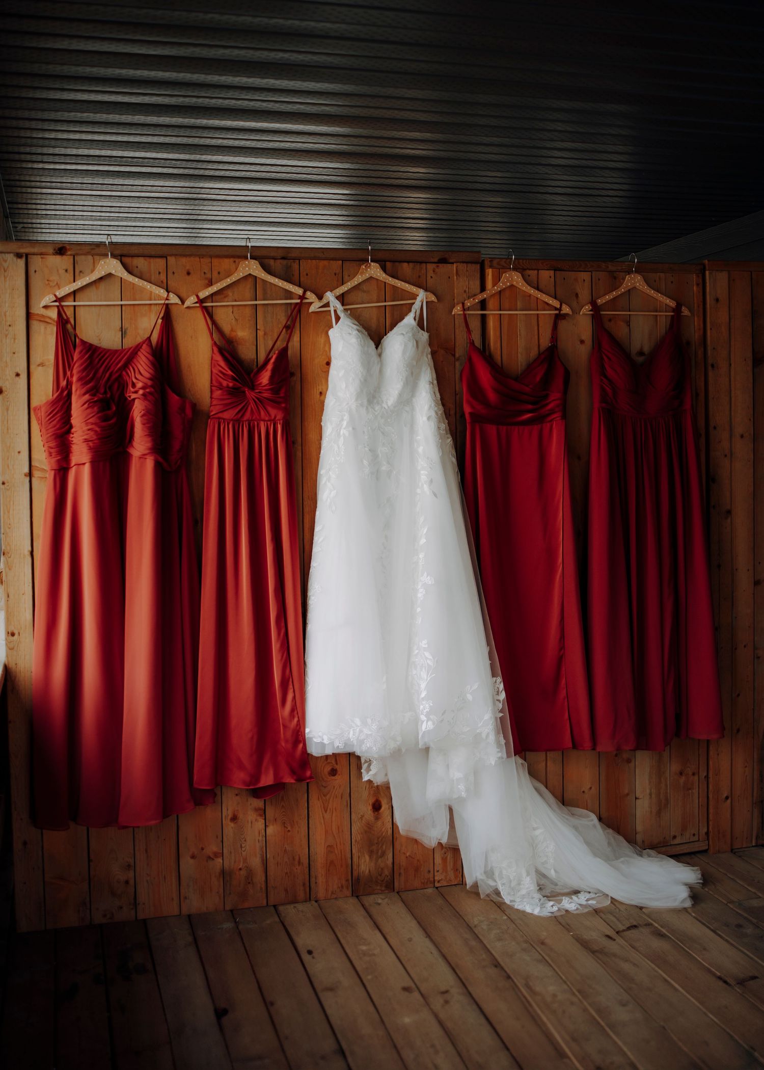 Wedding dresses in white and burgundy hanging in a row against wooden wall.