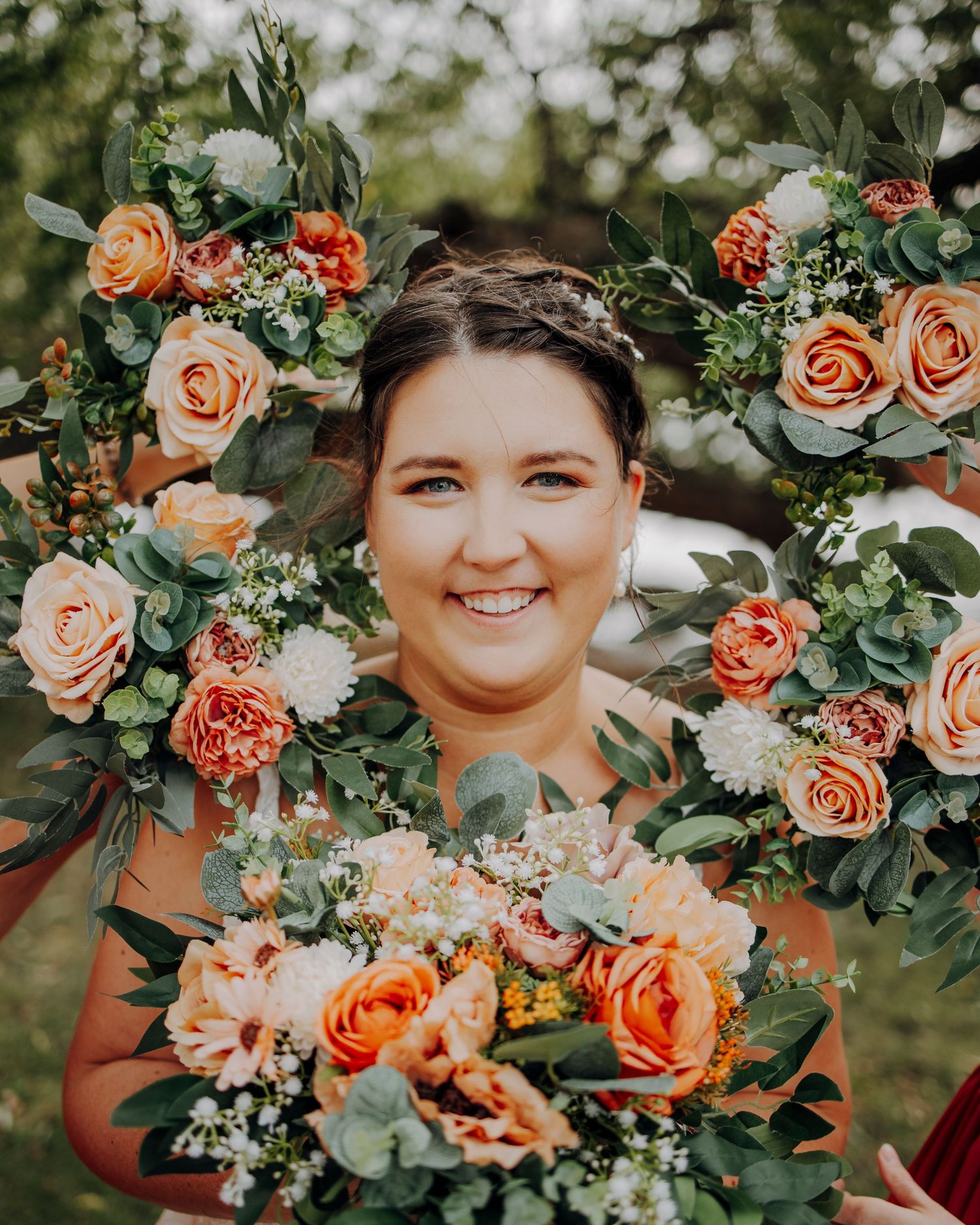 A wedding portrait framed by coral roses and greenery in natural outdoor lighting.