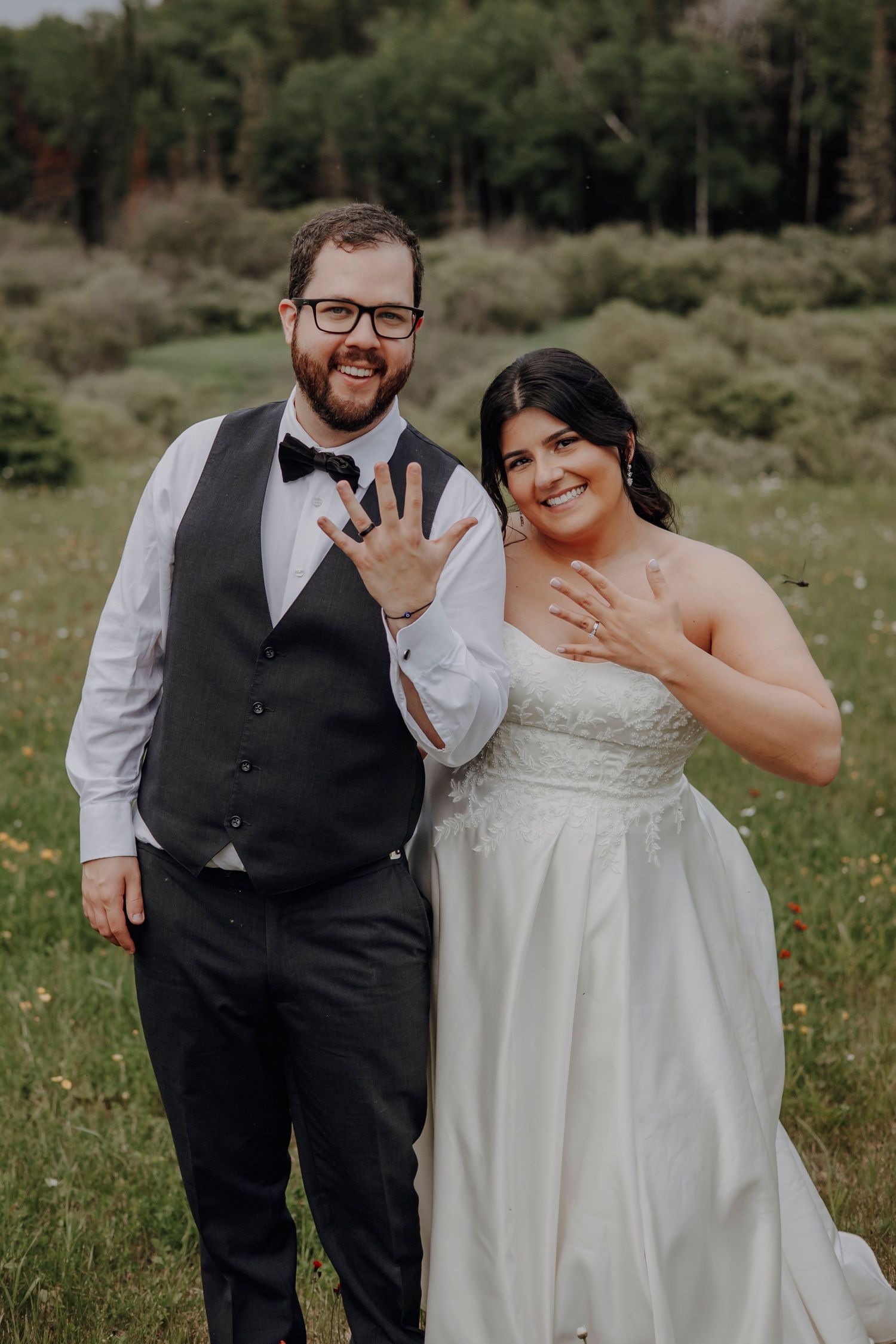Joyful wedding couple laughing together in outdoor field with wildflowers.
