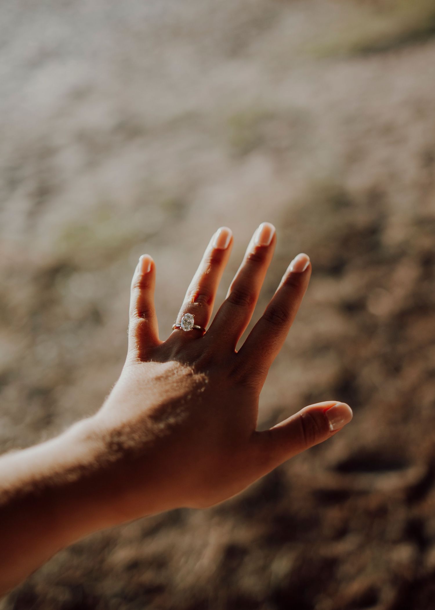Close-up shot of a hand displaying a new engagement ring against a soft blurred background.