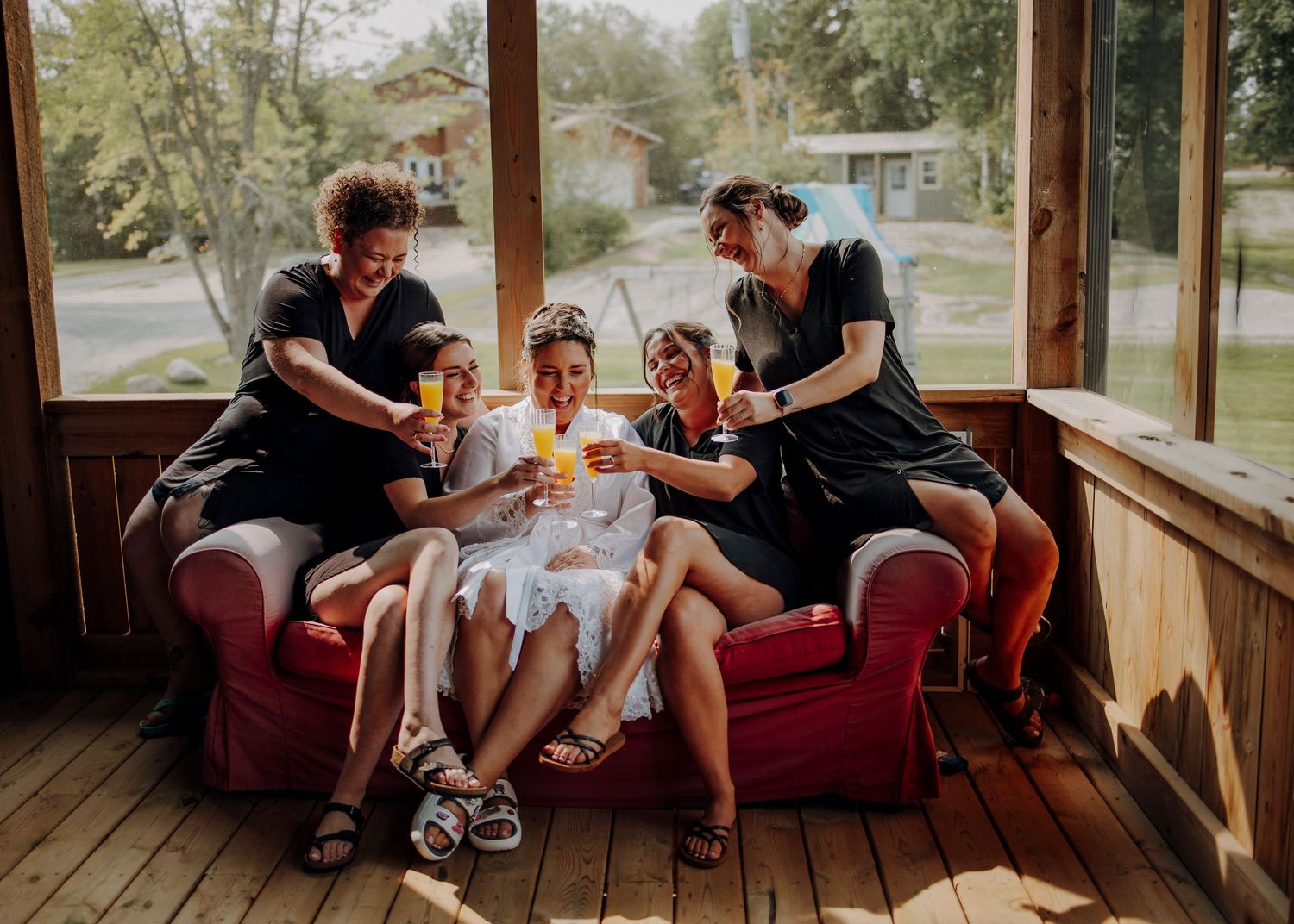 Family relaxing together on red couch on sunny porch while sharing snacks and drinks.