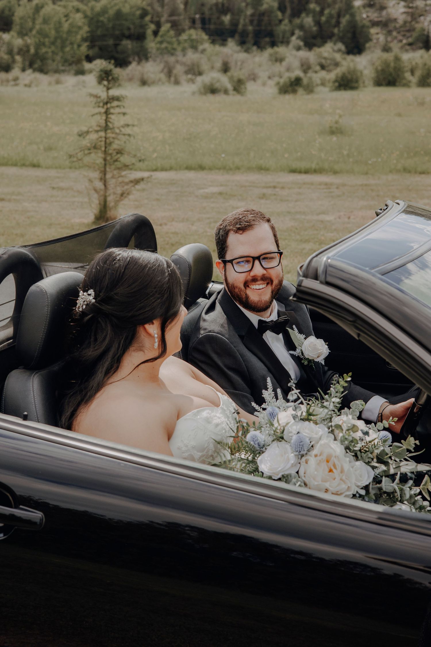 A couple sharing an intimate moment in a black car decorated with wedding flowers.
