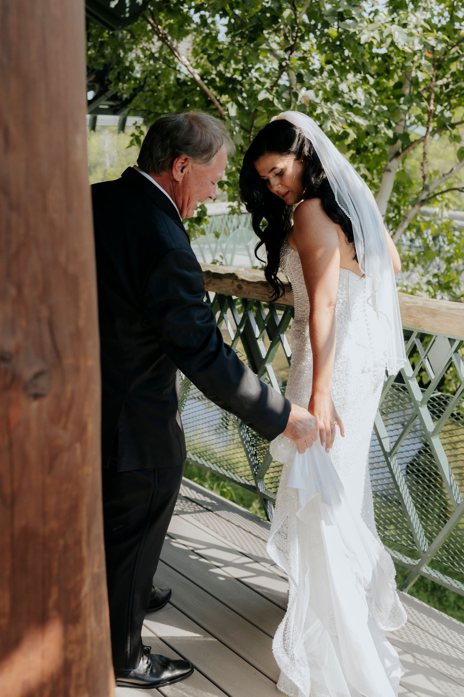 Wedding dress being adjusted on a wooden deck with trees in the background.