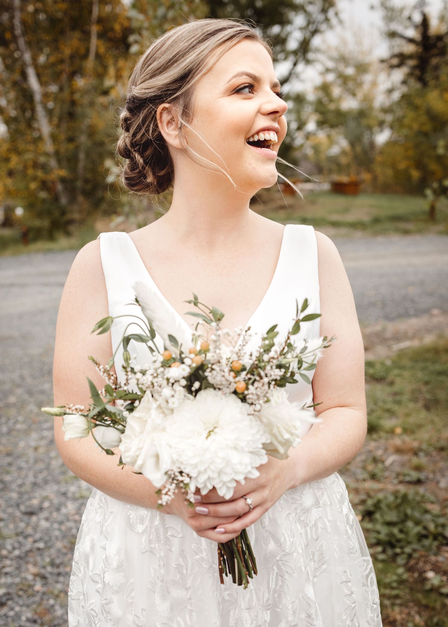 Bride holding white floral bouquet in lace dress during outdoor wedding.