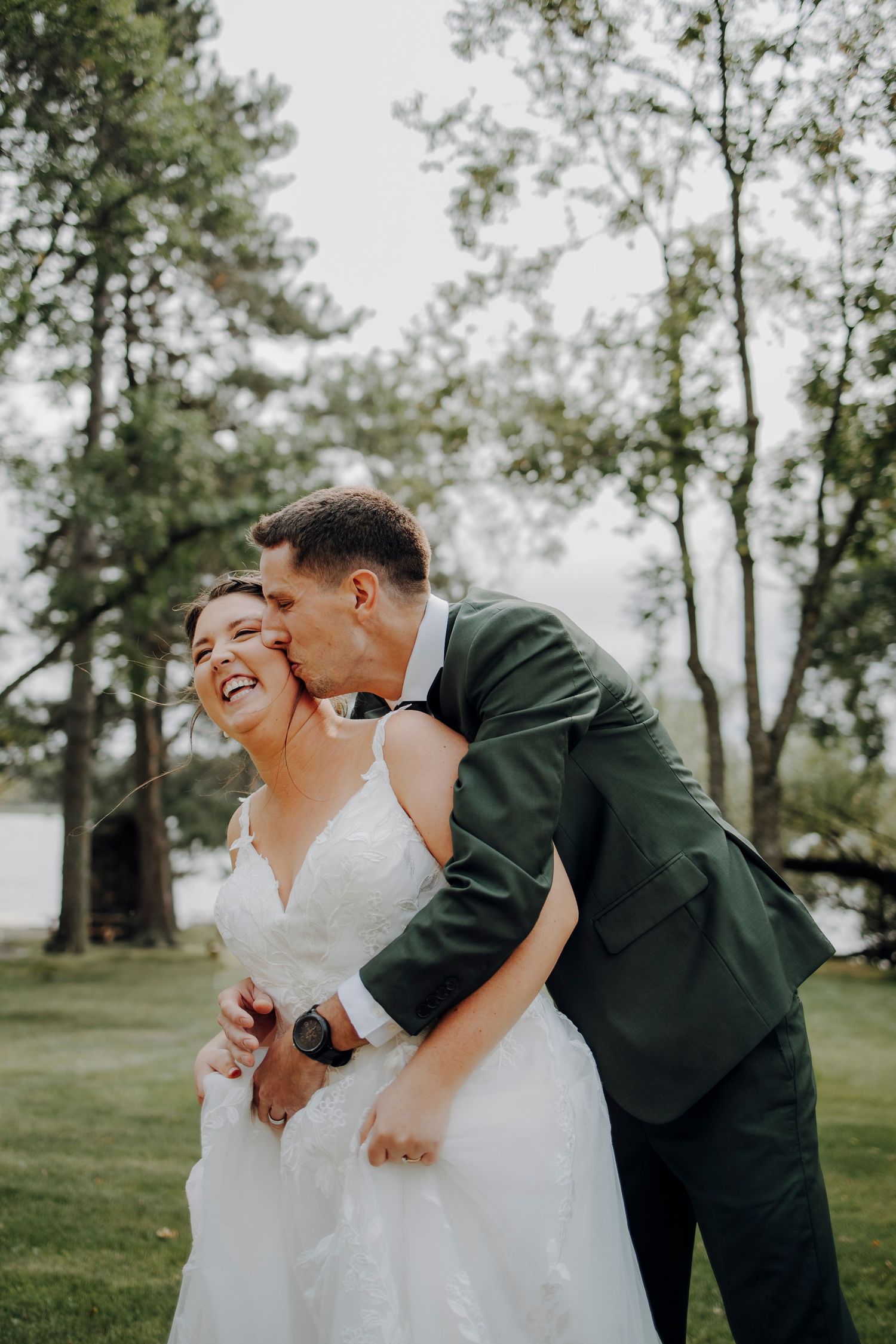 A joyful wedding couple shares candid laughing moments in an outdoor garden setting.