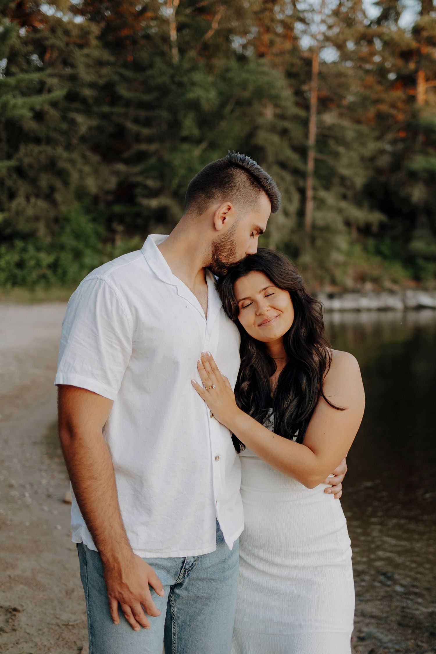 Romantic couple in white and denim embracing by a lake at sunset.