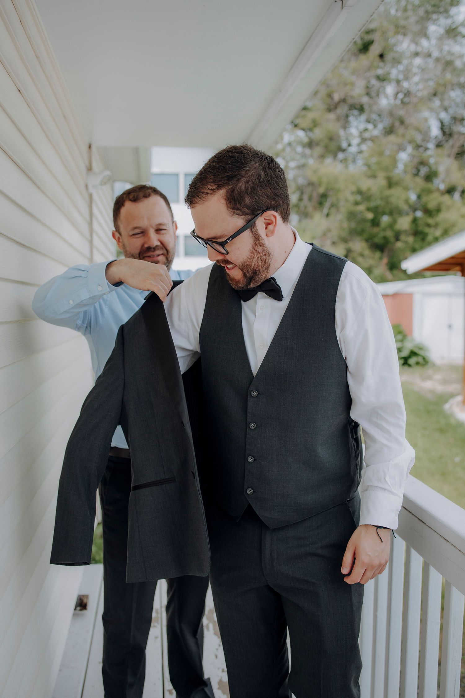 Two people in formal attire share a candid moment of laughter on a white porch.