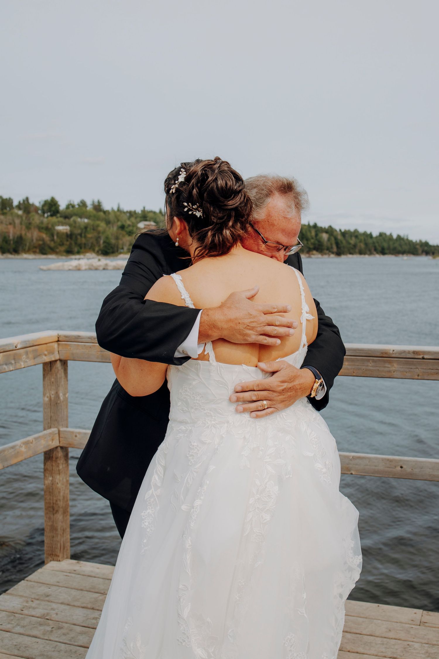Intimate wedding embraces captured on a waterfront dock with scenic lake views.
