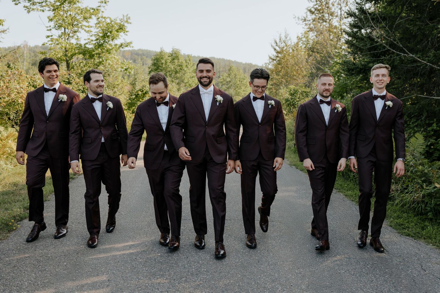 Groomsmen in black tuxedos walking together on outdoor path.