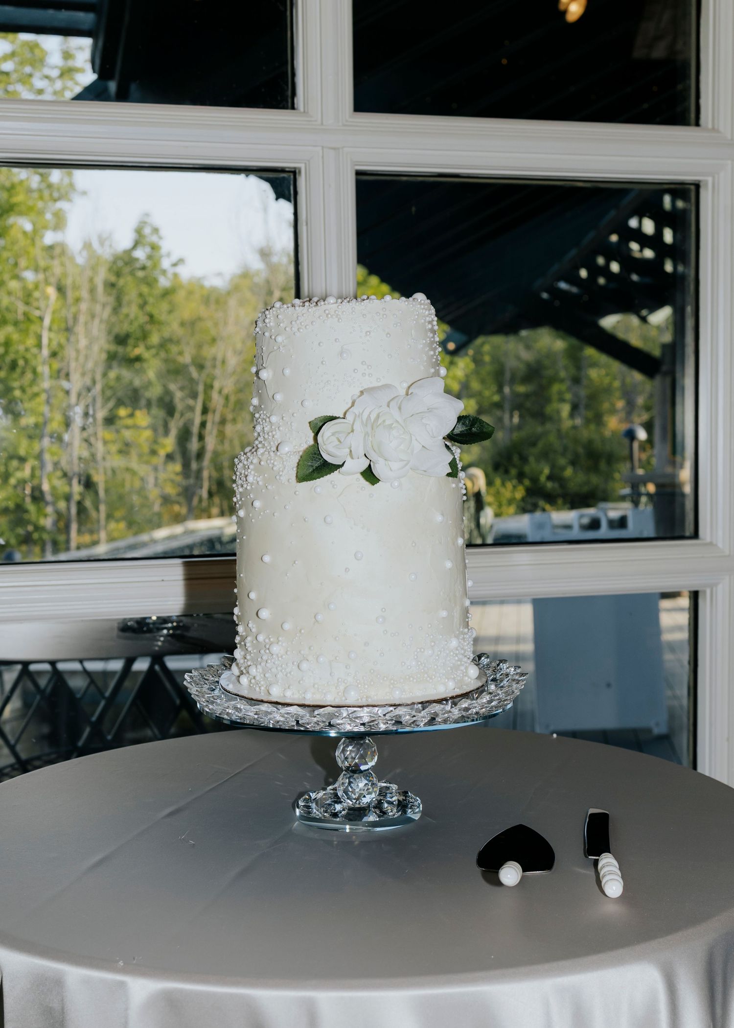 White tiered wedding cakes displayed on silver stands against window backdrop.