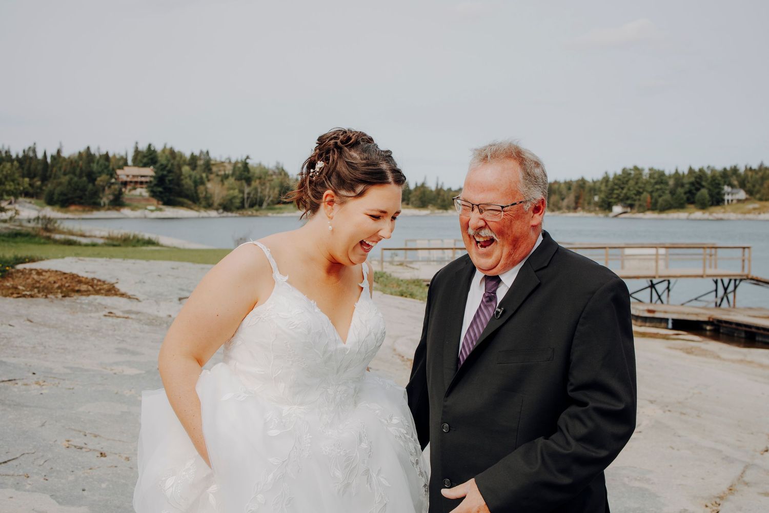 A joyful moment shared between two people on a lakeside dock during a wedding celebration.