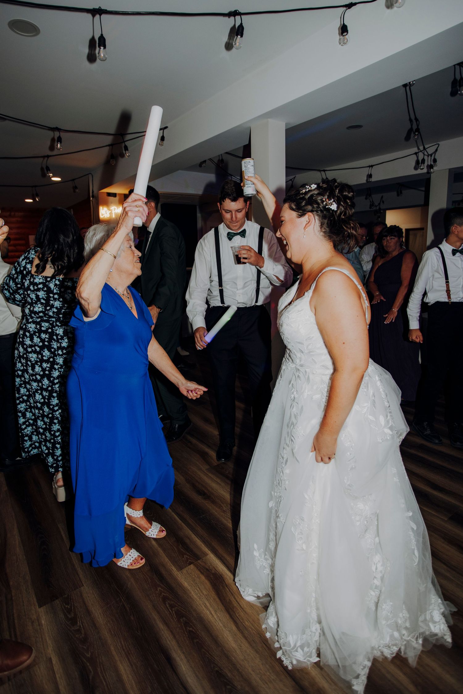 Wedding reception dancing with guests in formal attire on wooden dance floor.