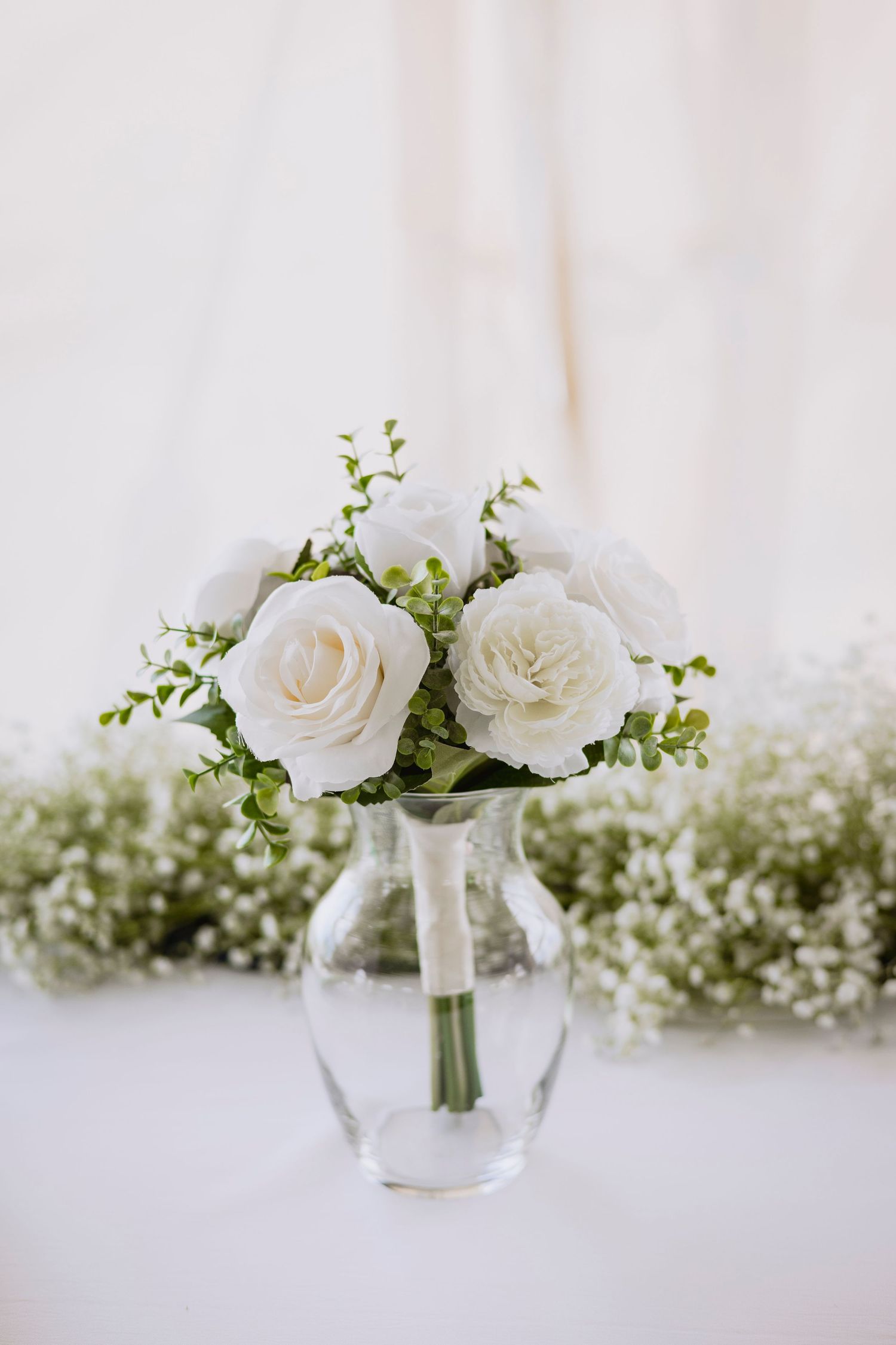 Simple white rose and greenery arrangement in clear glass vase with baby's breath accents.