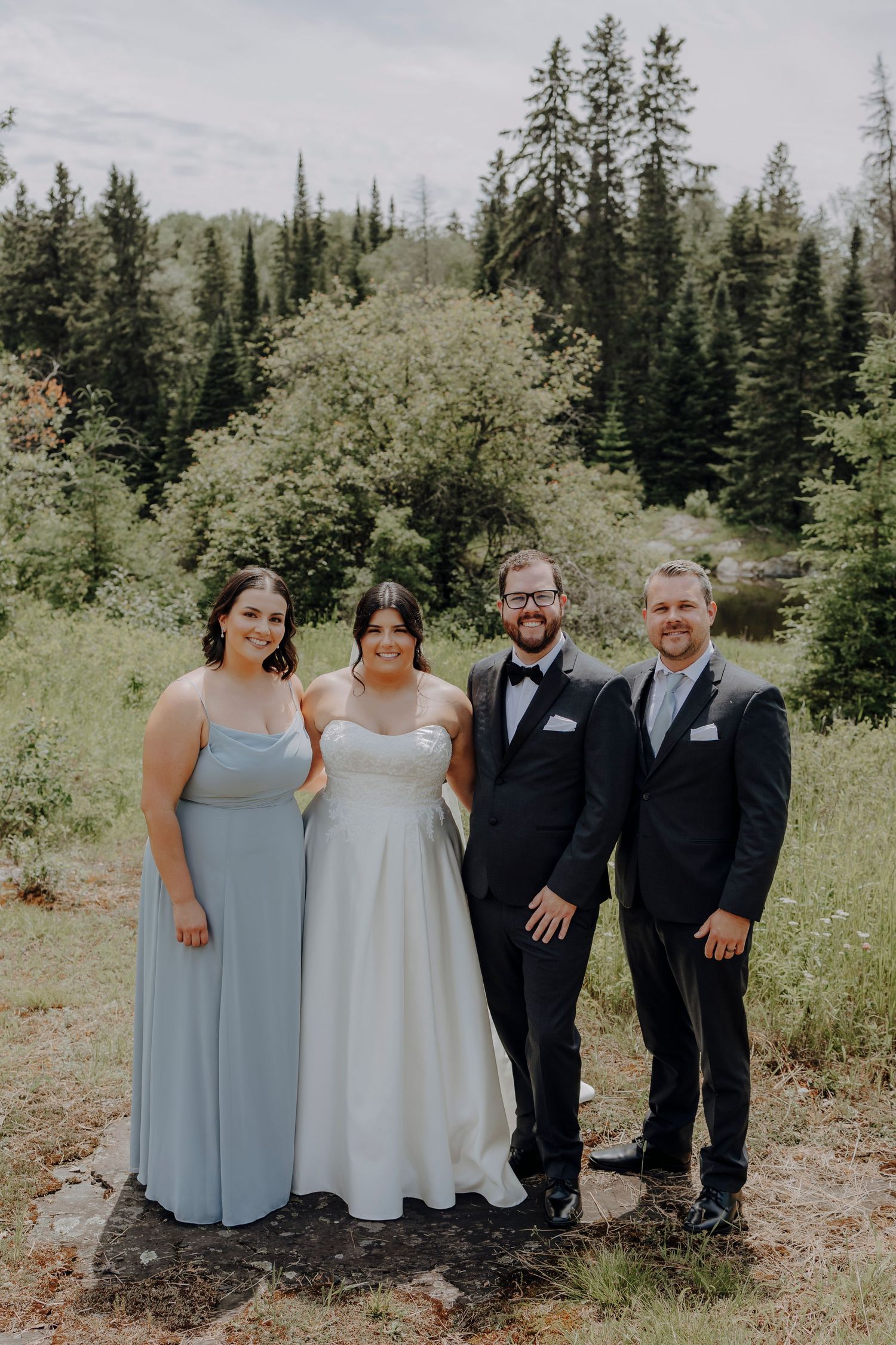 Wedding party members in coordinated gray and black attire pose together outdoors.
