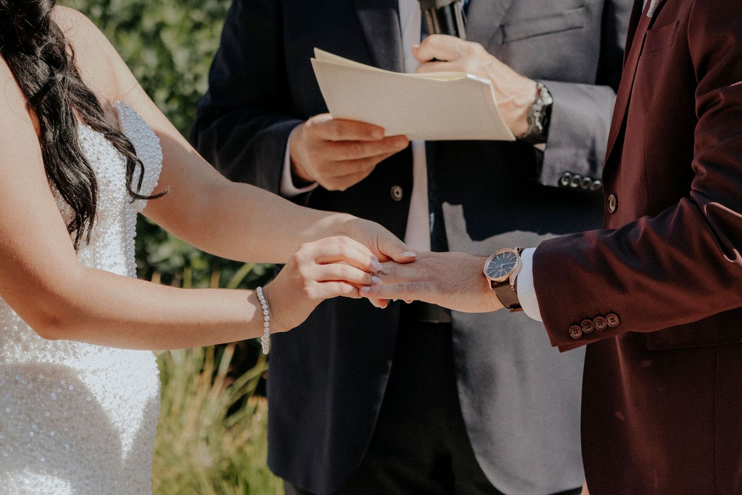 Close-up of hands exchanging rings during an outdoor wedding ceremony.