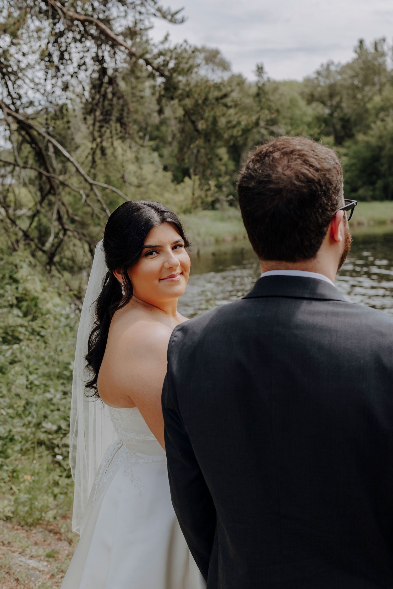 A couple shares intimate moments in a natural outdoor setting with trees and a lake in the background.