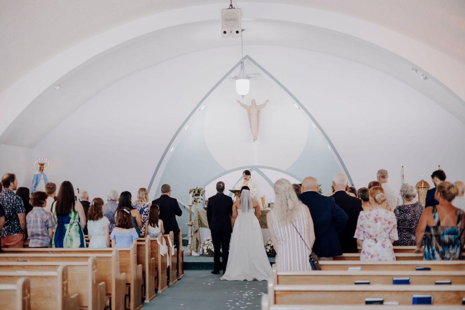 Interior shots of a white church or chapel with arched ceilings and rows of pews during a wedding ceremony.
