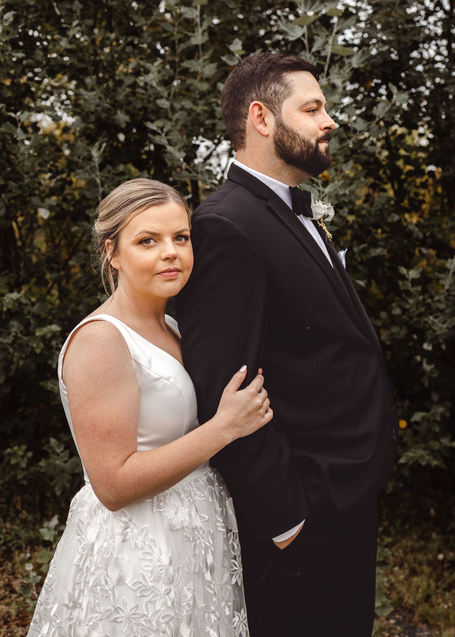 A wedding couple poses for a formal portrait against autumn trees and foliage.