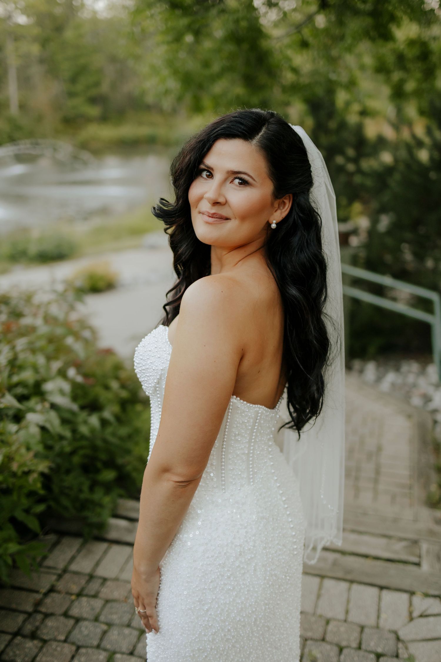 Bride in beaded white wedding dress poses in garden setting.