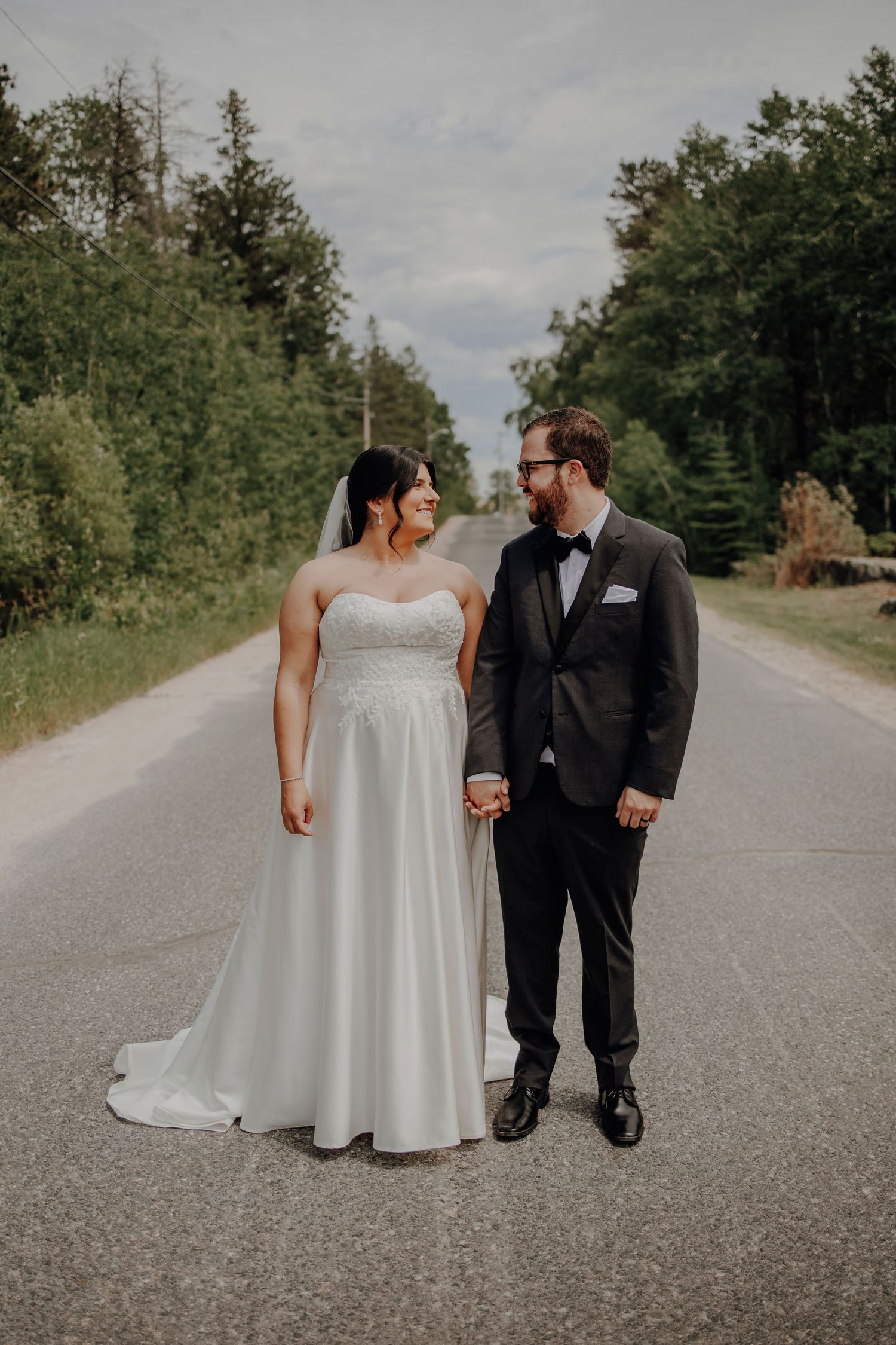 A romantic wedding photo series showing a couple walking together on a country road surrounded by trees.
