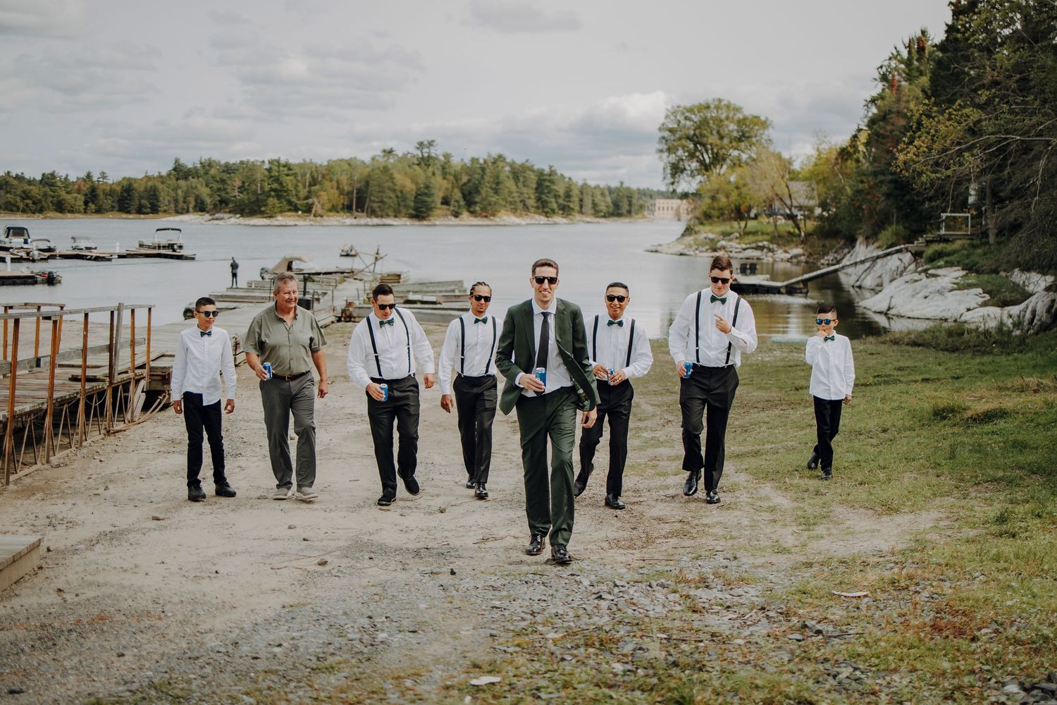 Wedding party in light gray and navy attire poses together on scenic waterfront dock during autumn celebration.