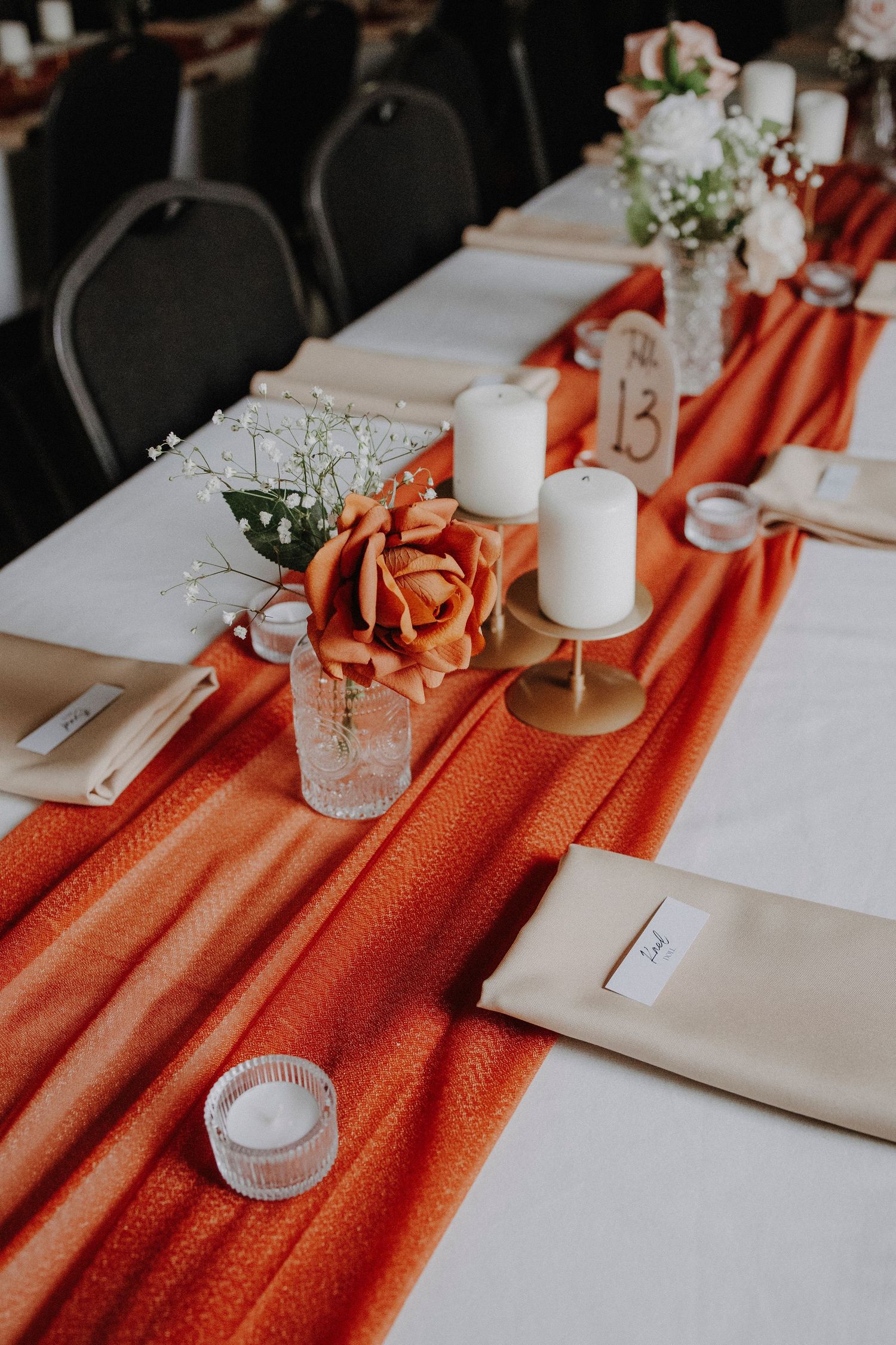 Wedding reception table decorated with orange runner, white candles, and delicate baby's breath flowers.