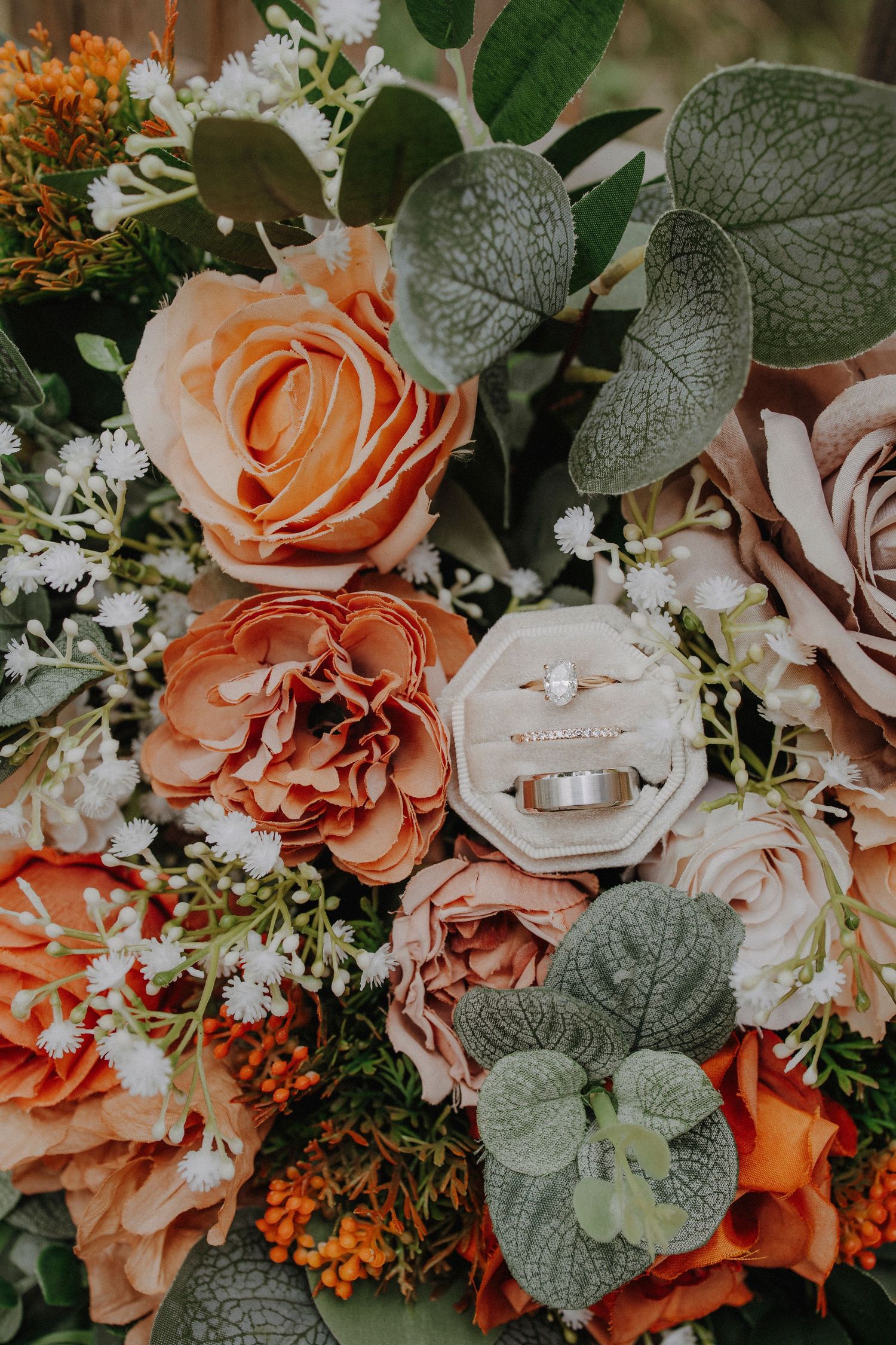 Peach and coral roses with silver dollar eucalyptus leaves surround wedding rings.