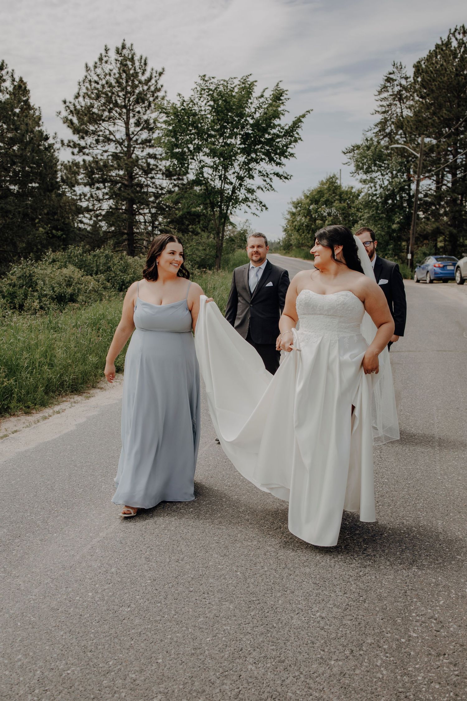 Wedding party walking and laughing together on a paved path with trees in the background.