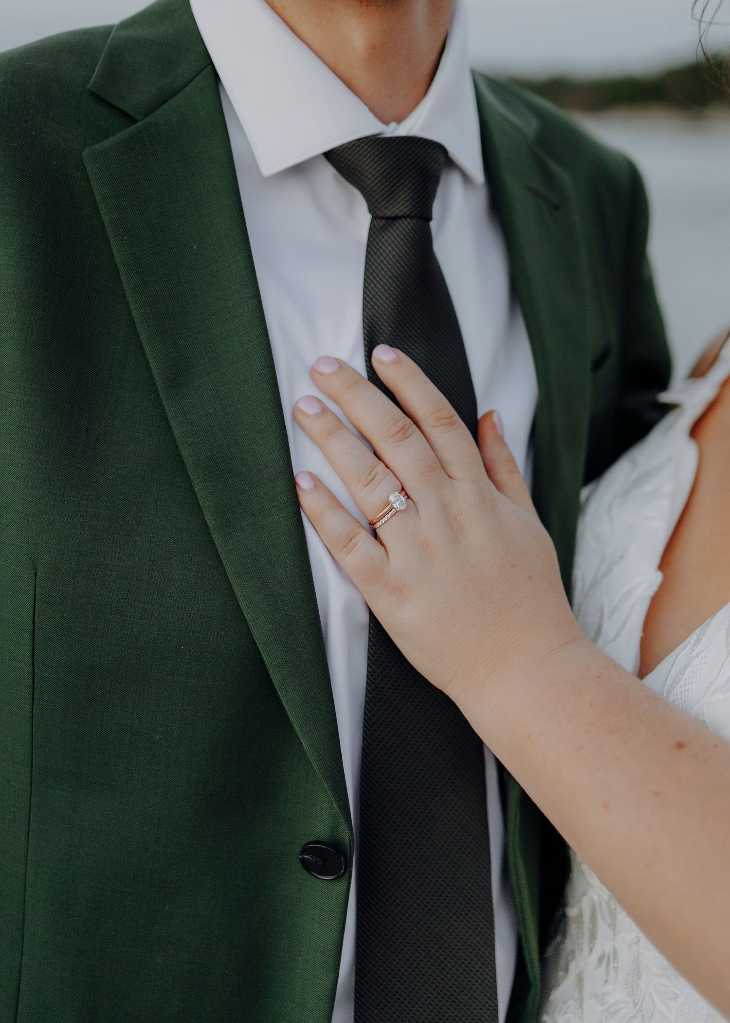 Close-up of hands showing wedding ring against dark green suit jacket.
