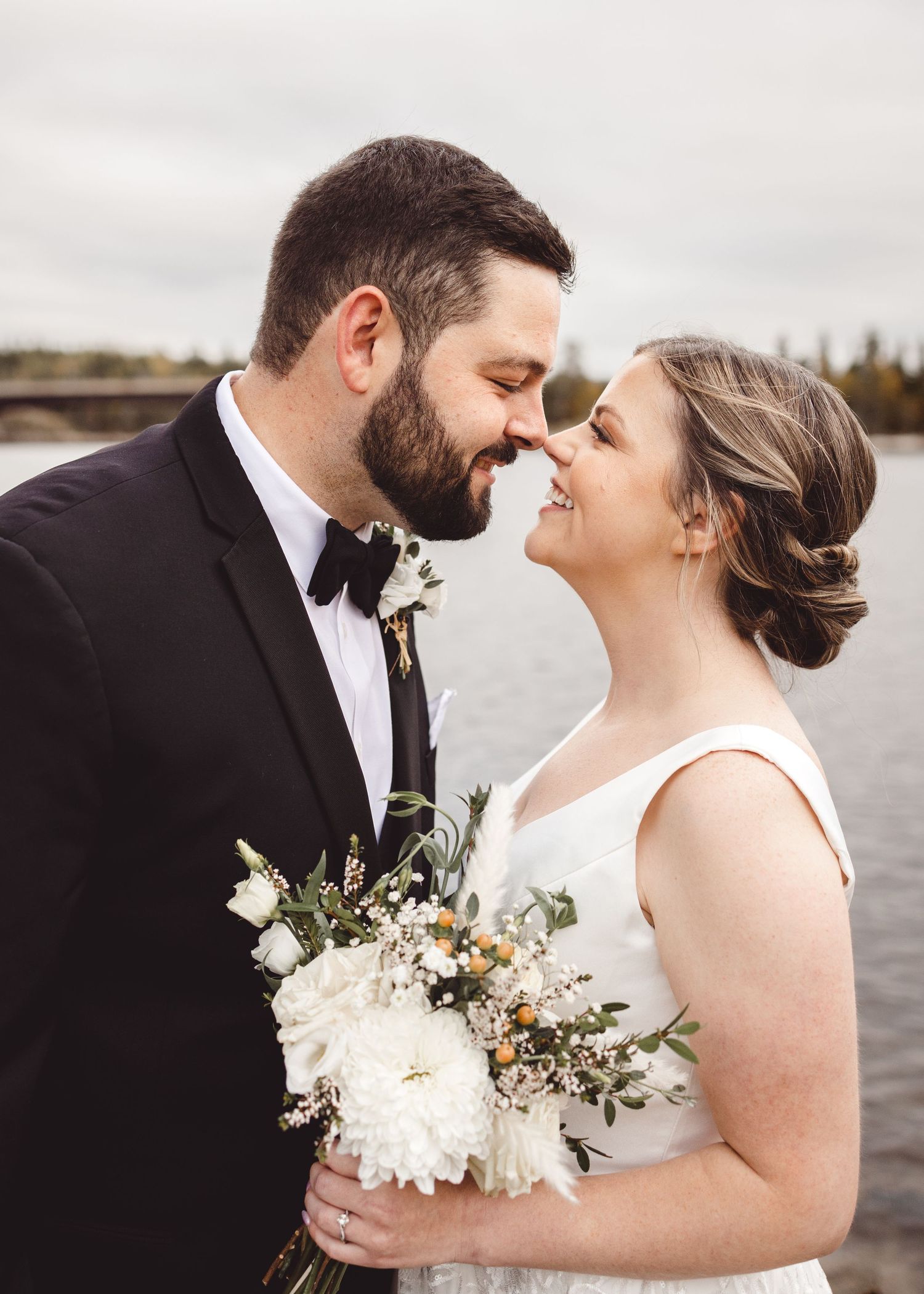 Close up of newlyweds sharing an intimate moment with white floral bouquet by waterfront.