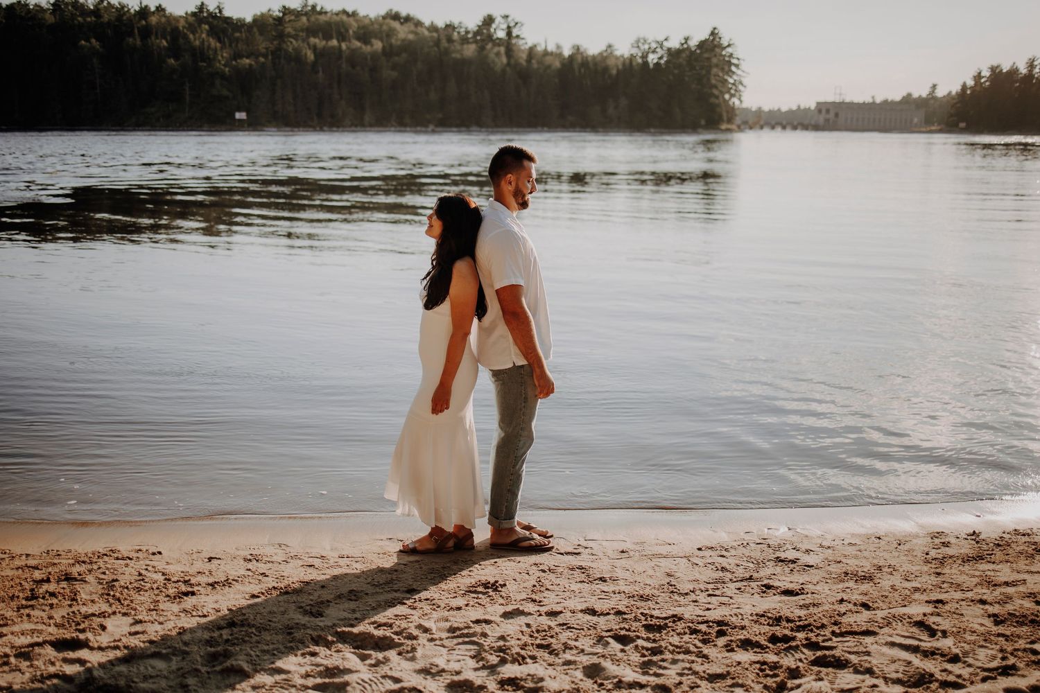 A couple standing at the water's edge on a beach during sunset.