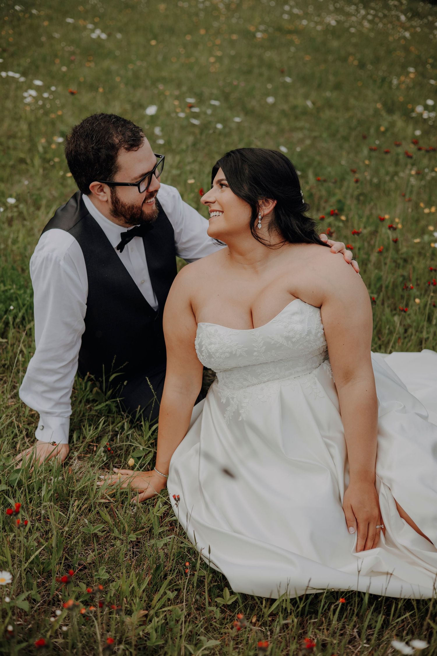 Candid wedding photos of couple sharing intimate moments while sitting in a wildflower meadow.