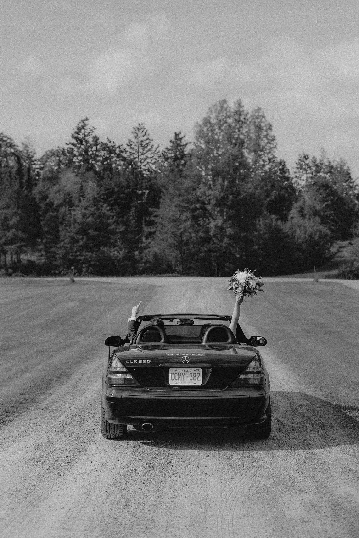 A black Mercedes decorated with wedding flowers parked on a rural road.
