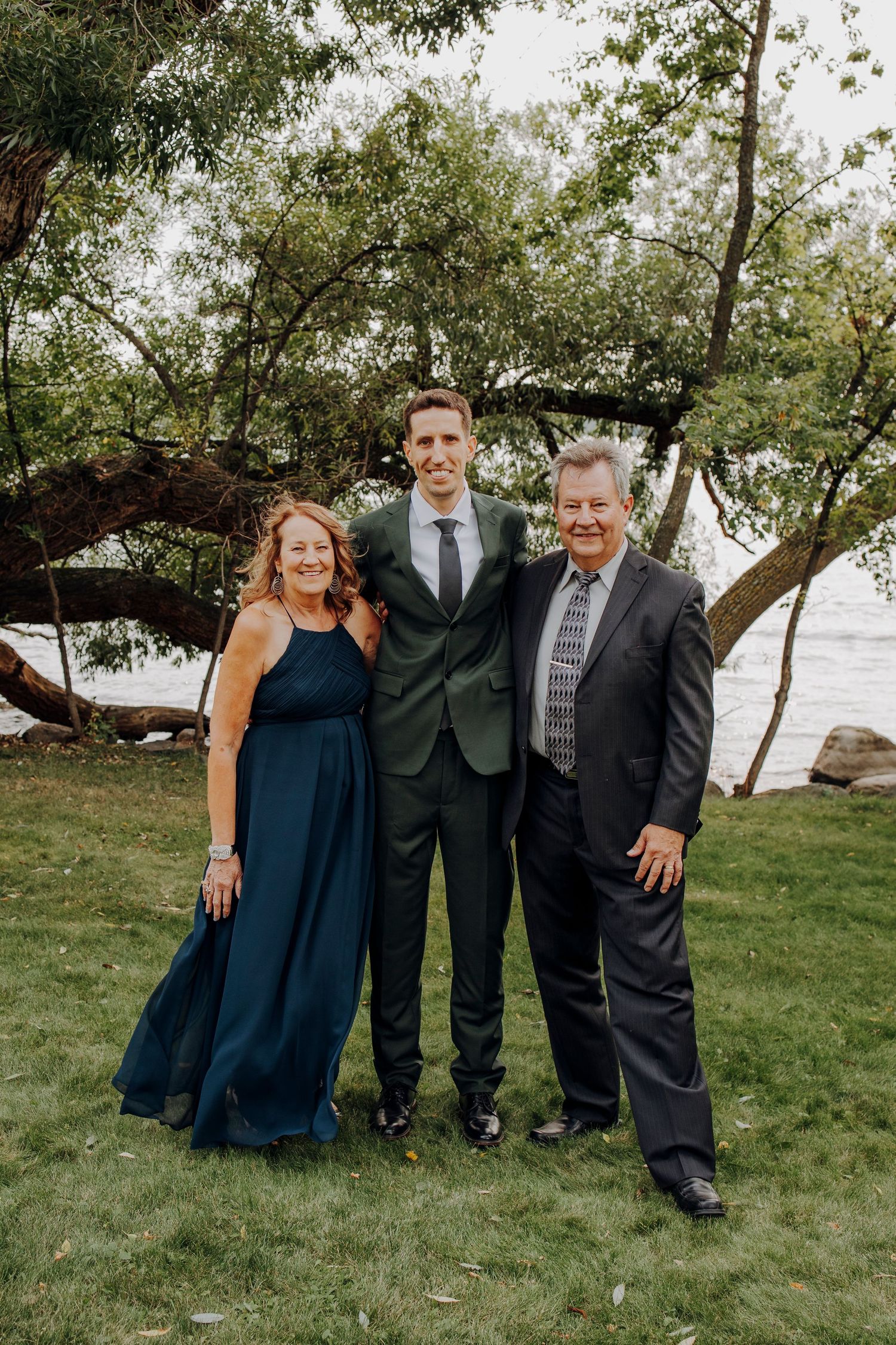 Wedding party portrait with green suit and navy dress against waterfront backdrop.