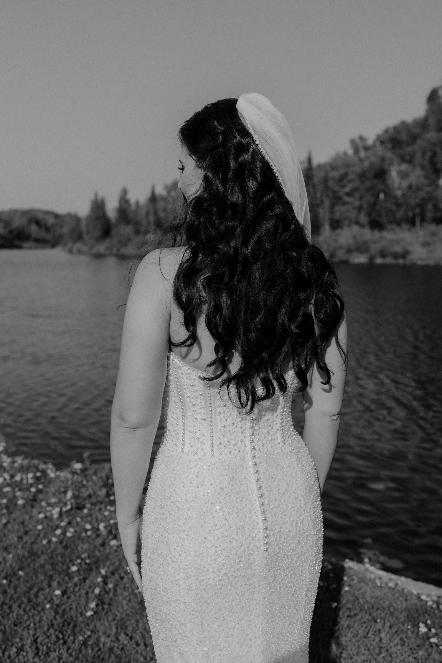 Close-up detail of a beaded wedding dress back against a lakeside backdrop.