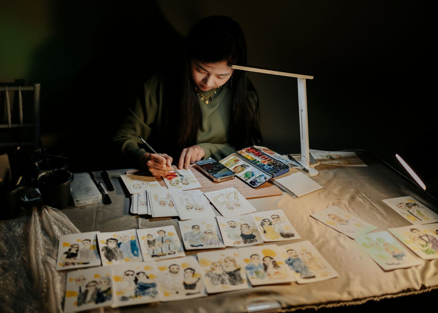 A person working late at night sorting through printed photographs under desk lamp lighting.