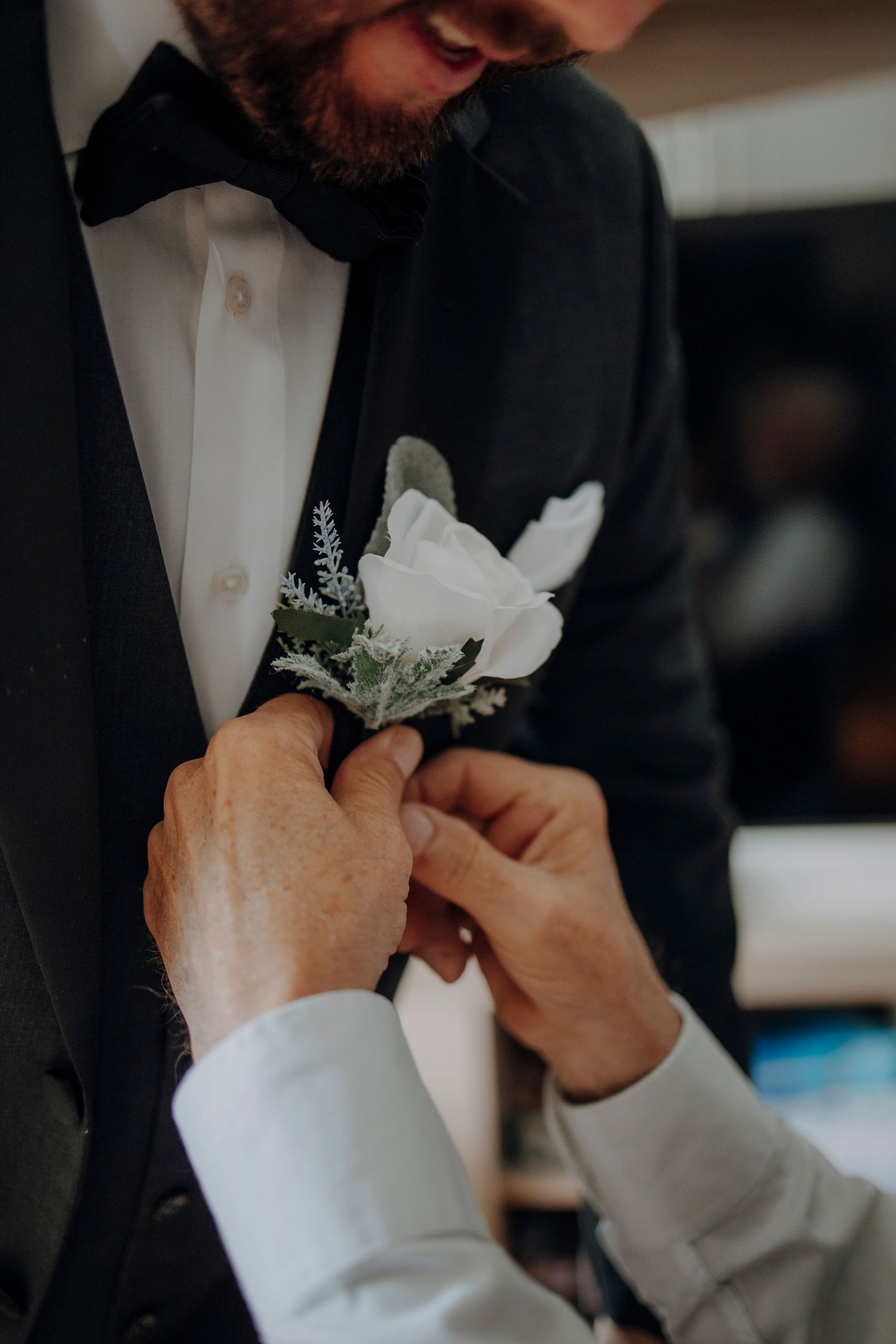 Close-up of groom adjusting white floral boutonniere on black suit jacket lapel.