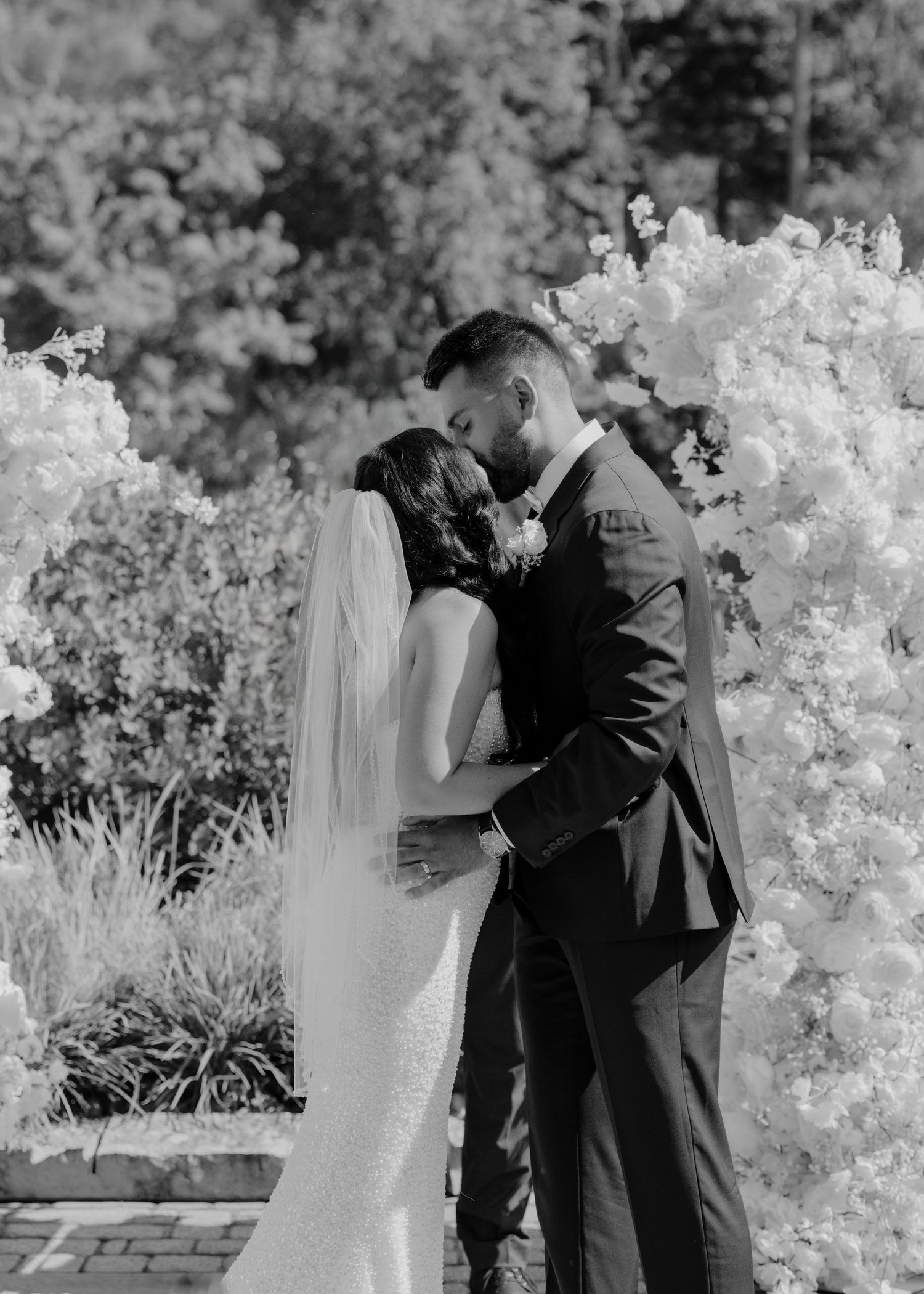Romantic black and white wedding photo with couple embracing among white flowering trees.
