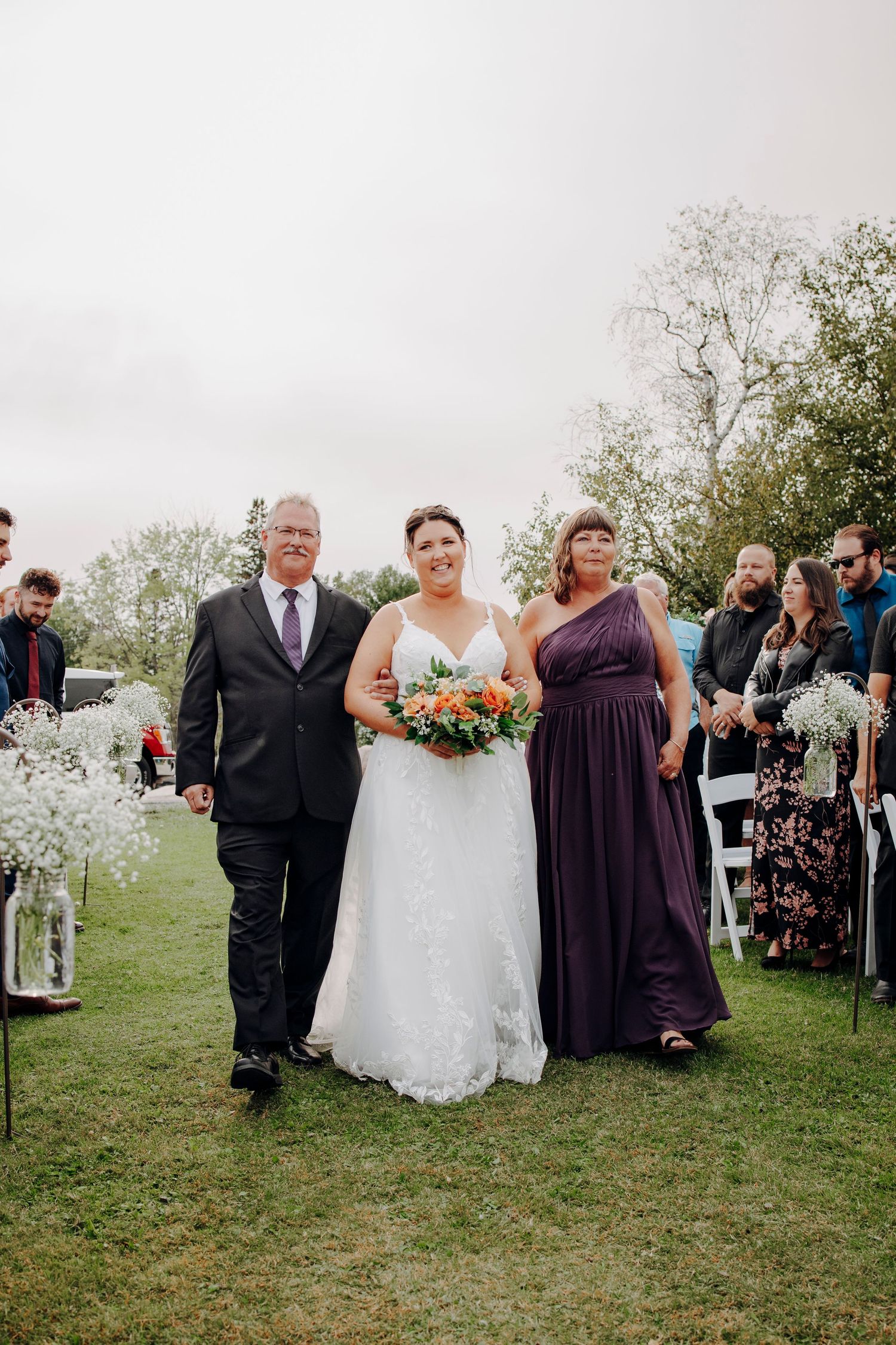 Wedding party gathered outdoors with purple bridesmaid dresses and floral arrangements.
