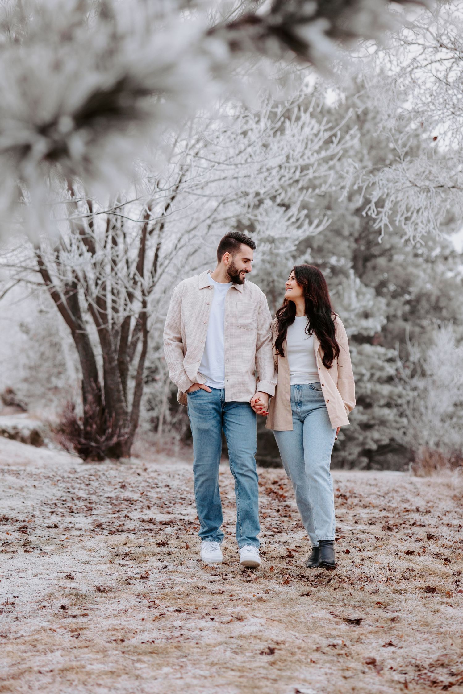 Couple in matching light sweaters walking together on a frosty winter path.