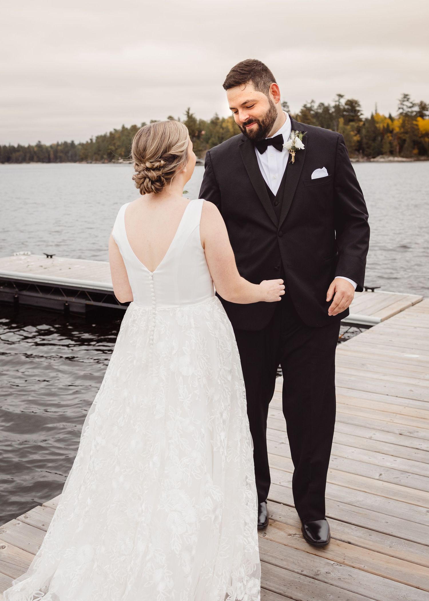 A romantic moment between newlyweds on a wooden dock overlooking a serene lake.