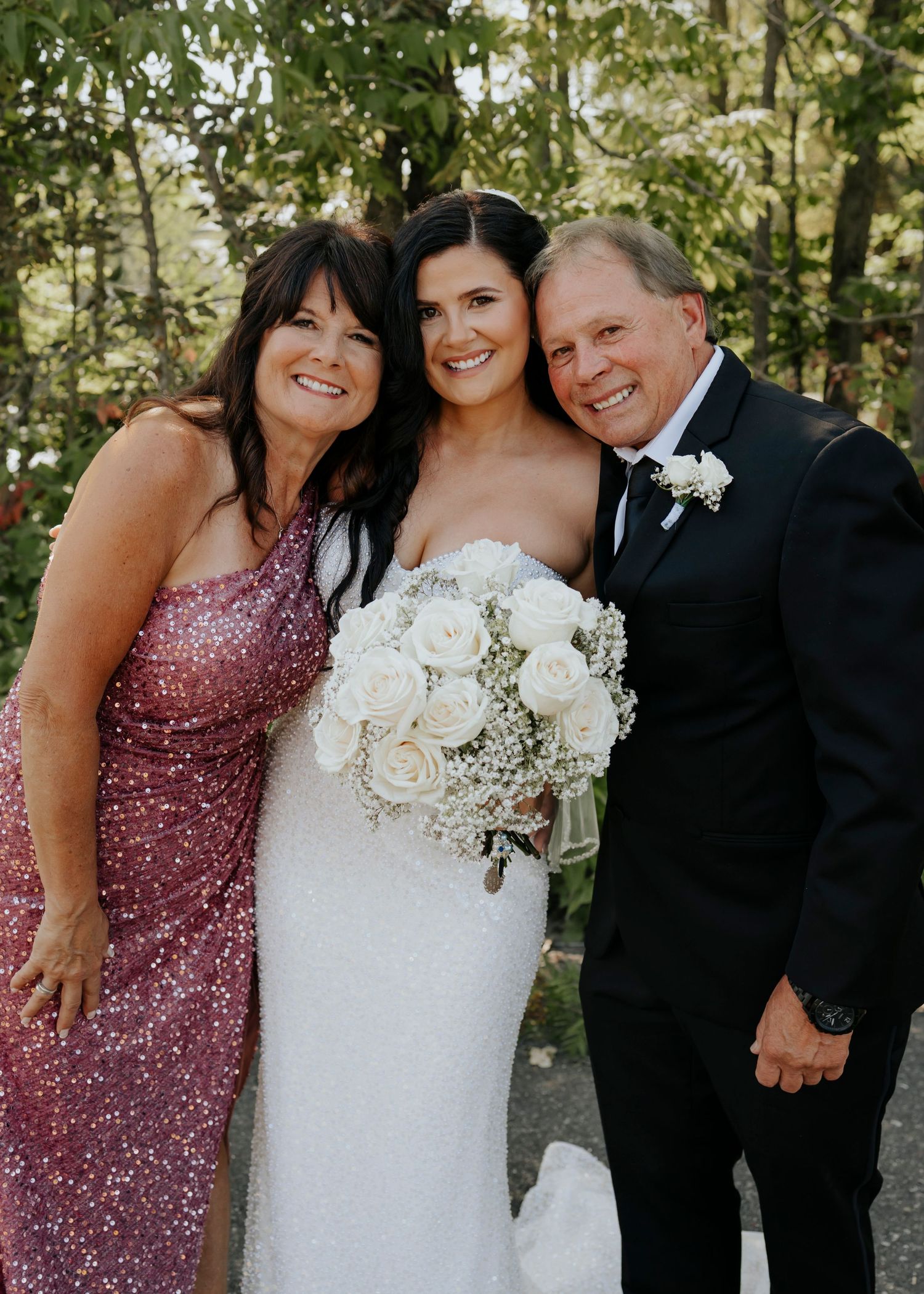 Wedding party members in sparkly pink dresses and formal attire posing together outdoors.