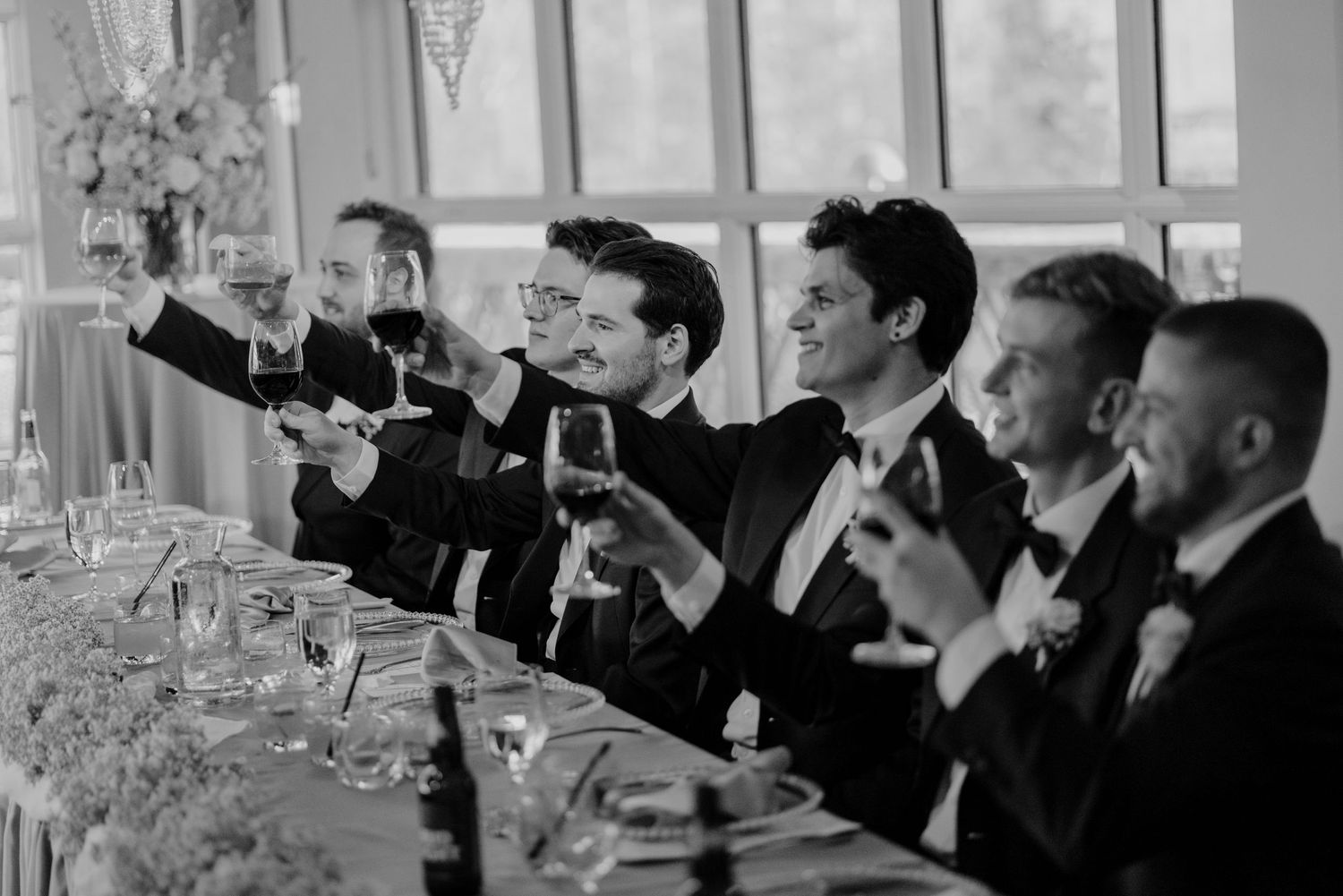 Wedding reception guests in formal attire raising glasses for a celebratory toast.