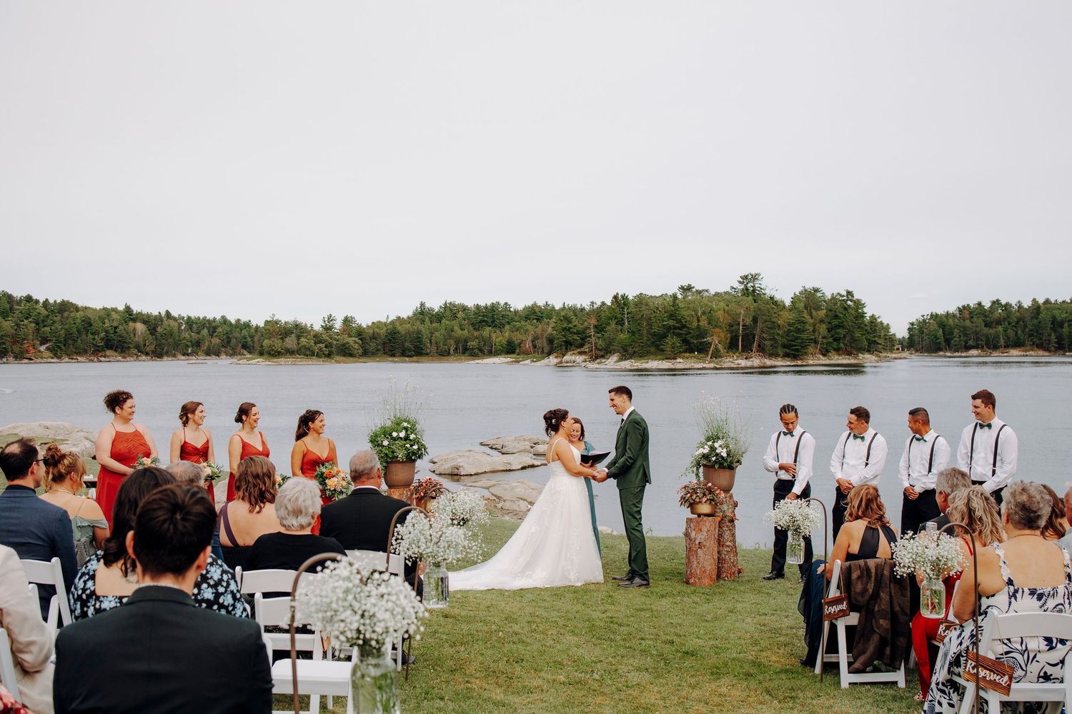 Panoramic view of outdoor wedding ceremony setup by lakeside with guests seated.
