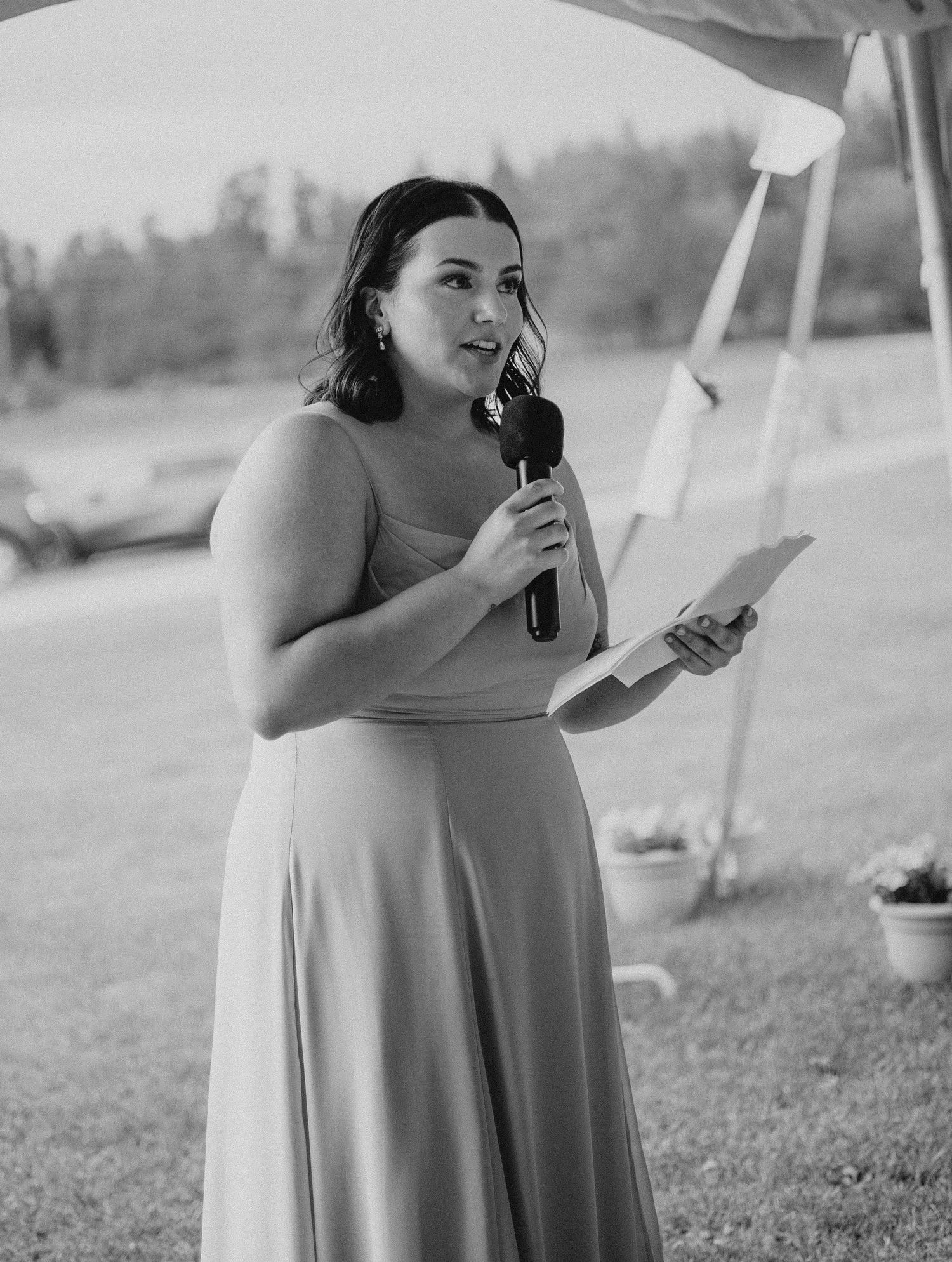 Black and white image shows someone holding a compact mirror during outdoor wedding preparations.
